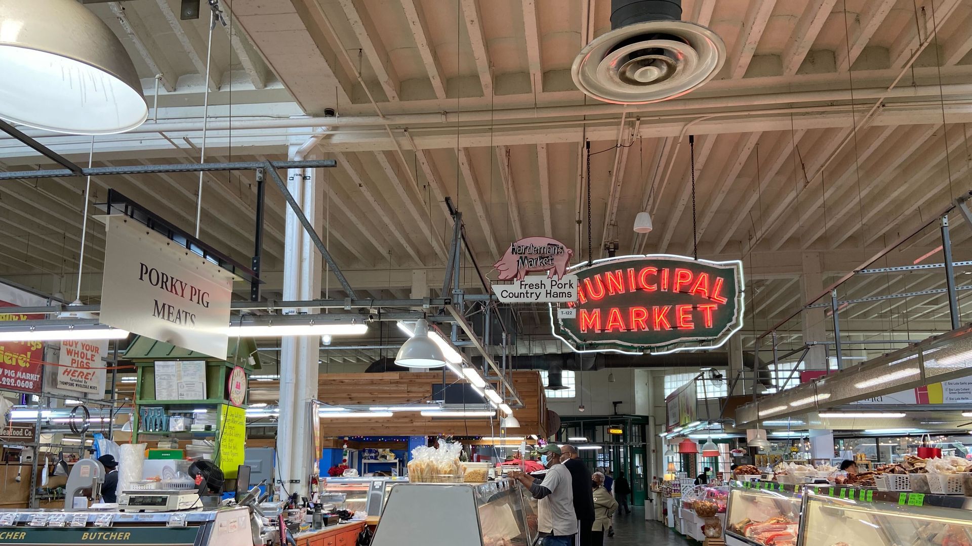 A photo of an old-fashioned municipal market with food and butcher stands. A neon "Municipal Market" sign hangs from the ceiling