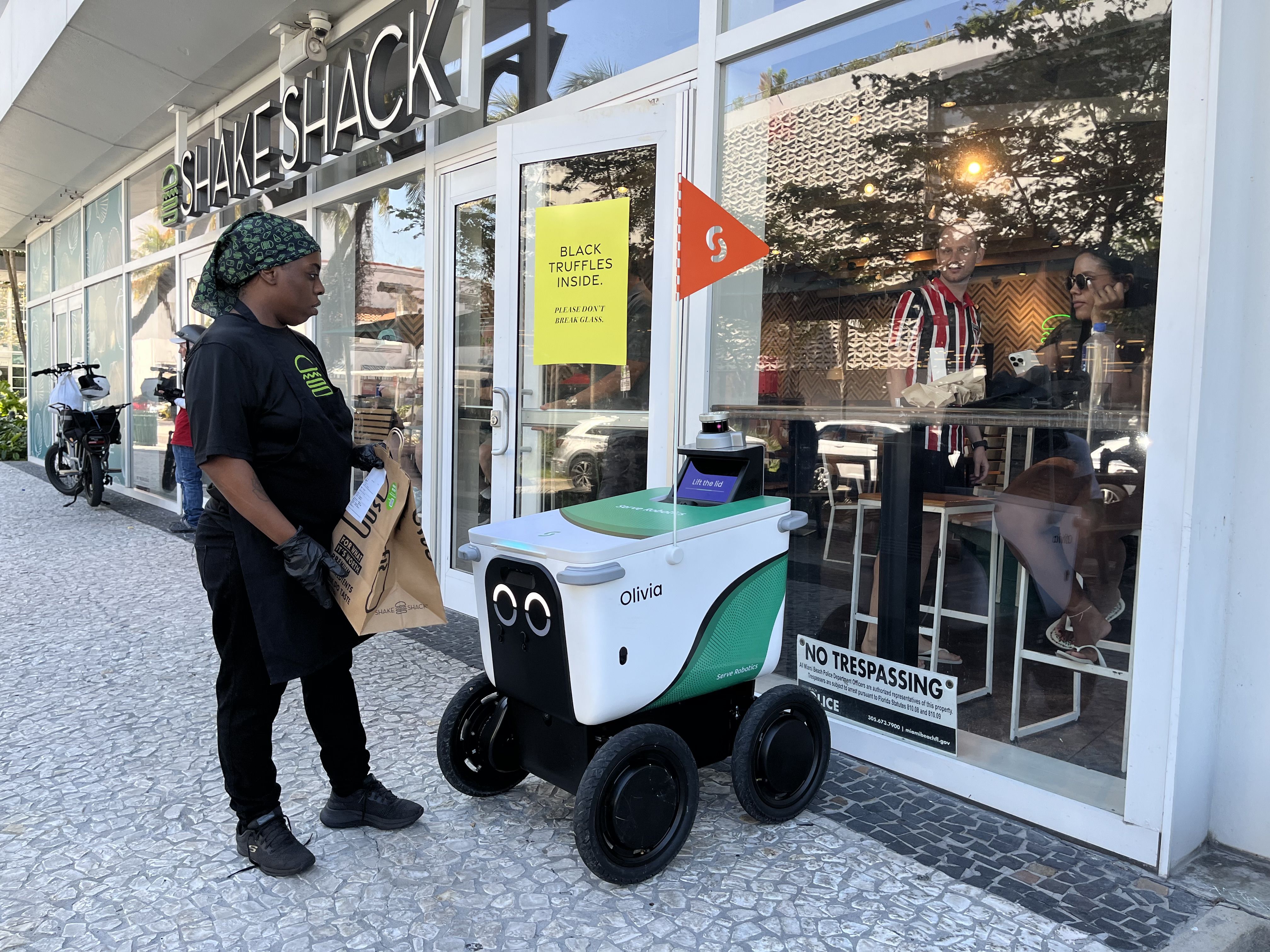 A Shake Shack employee puts an order inside Olivia the robot's cargo hold.