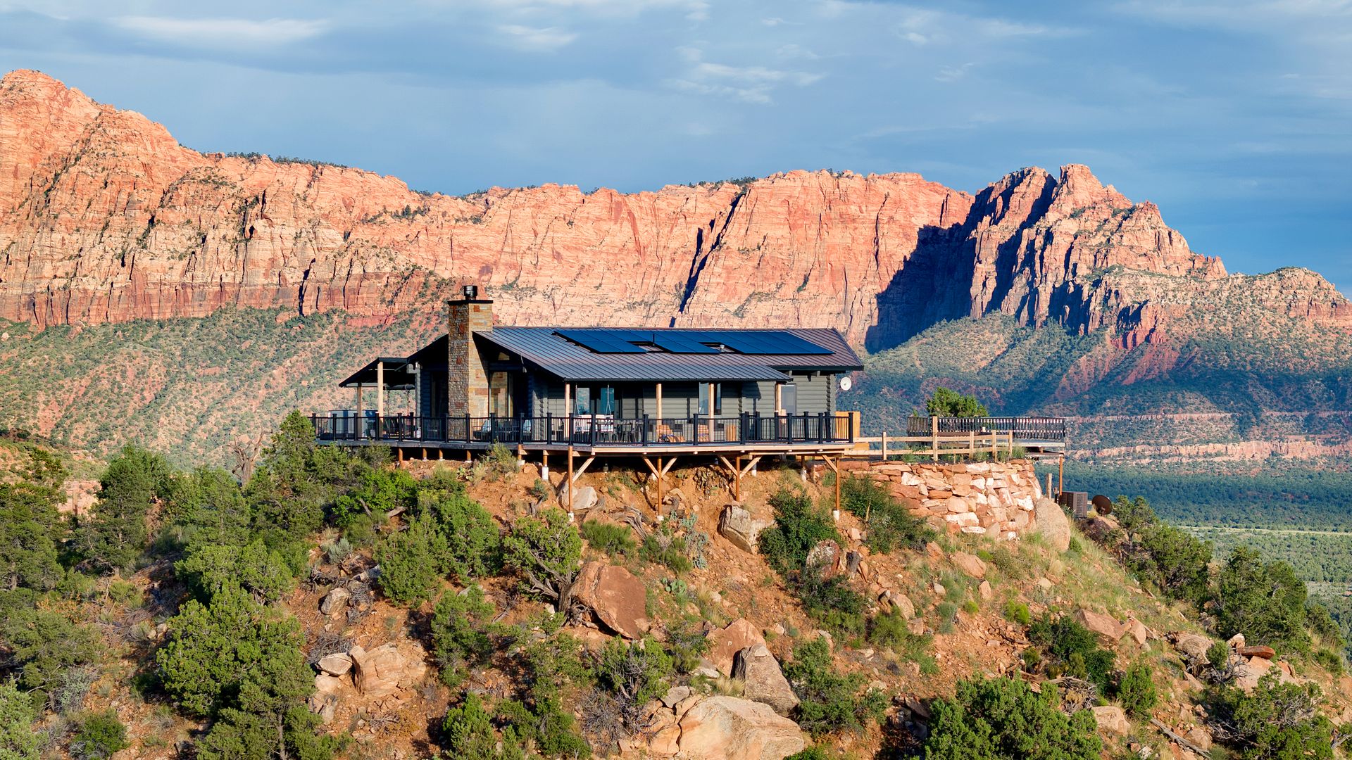 A wood house on a desert hill with red rock bluffs in the background.