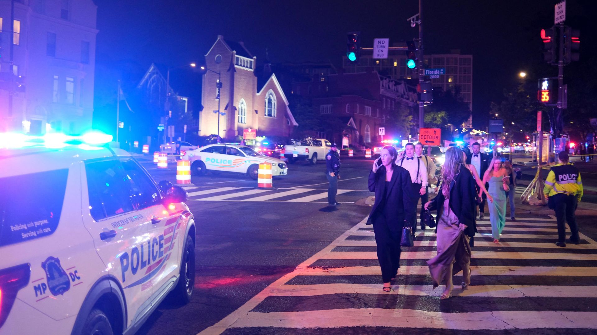 Dinnergoers in gowns and tuxedos walk down Connecticut Avenue surrounded by police