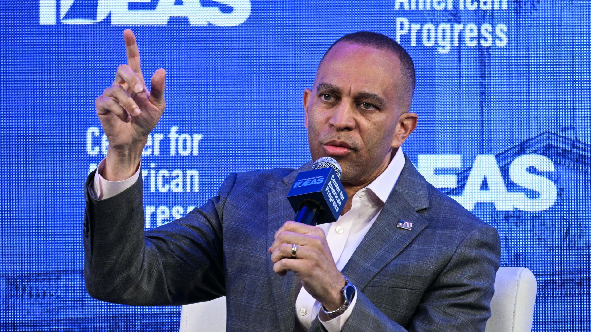 Man in a blue plaid suit speaks into a microphone on a blue backdrop reading "IDEAS" and "Center for American Progress".