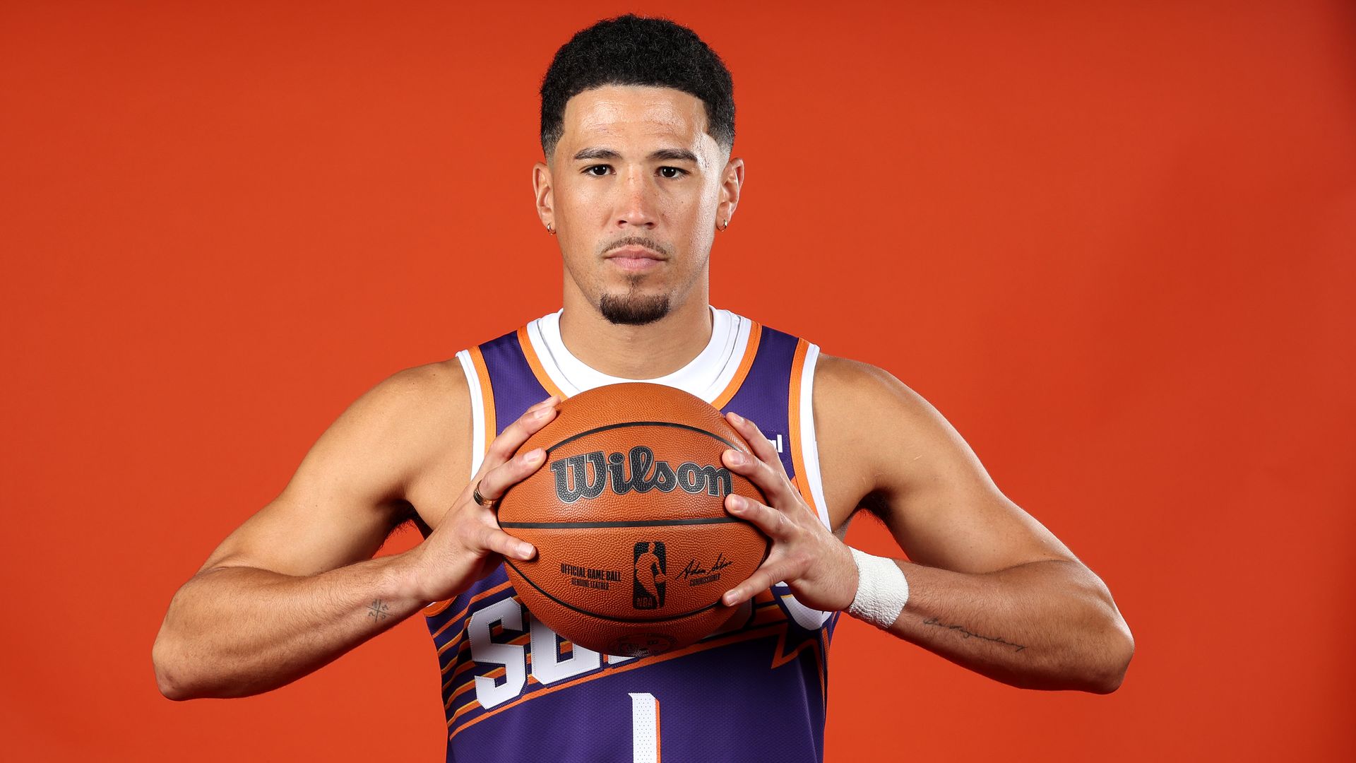 A basketball player in a Suns jersey posing for a photo while holding a basketball. 
