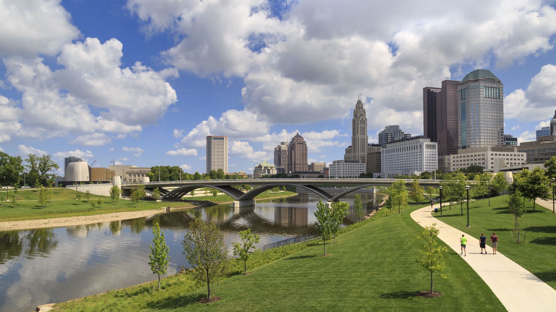 Columbus skyline in background among fluffy clouds, with Scioto Mile park greenspace and walking path in foreground