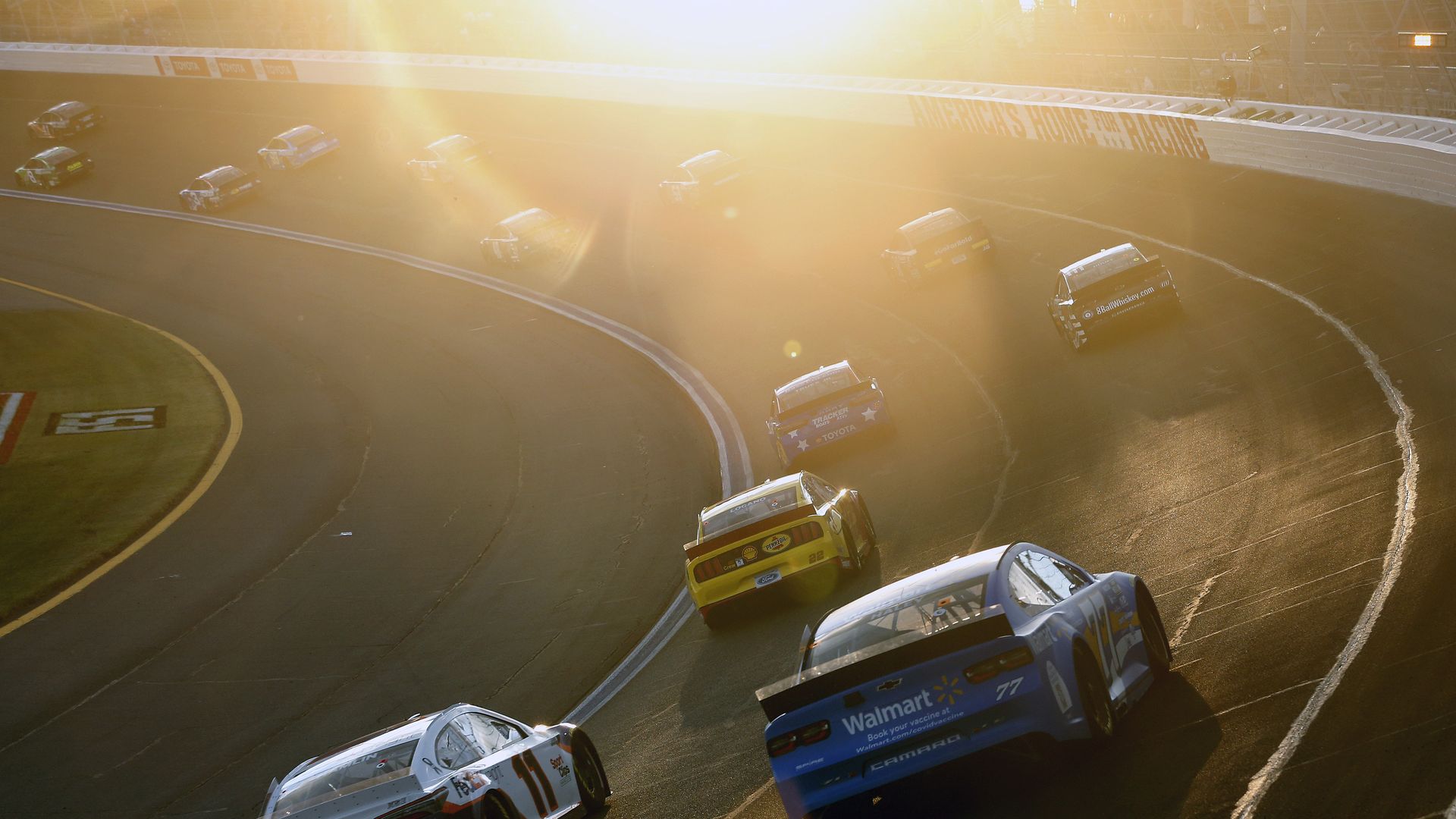 nascar cars driving around a track as the sun sets
