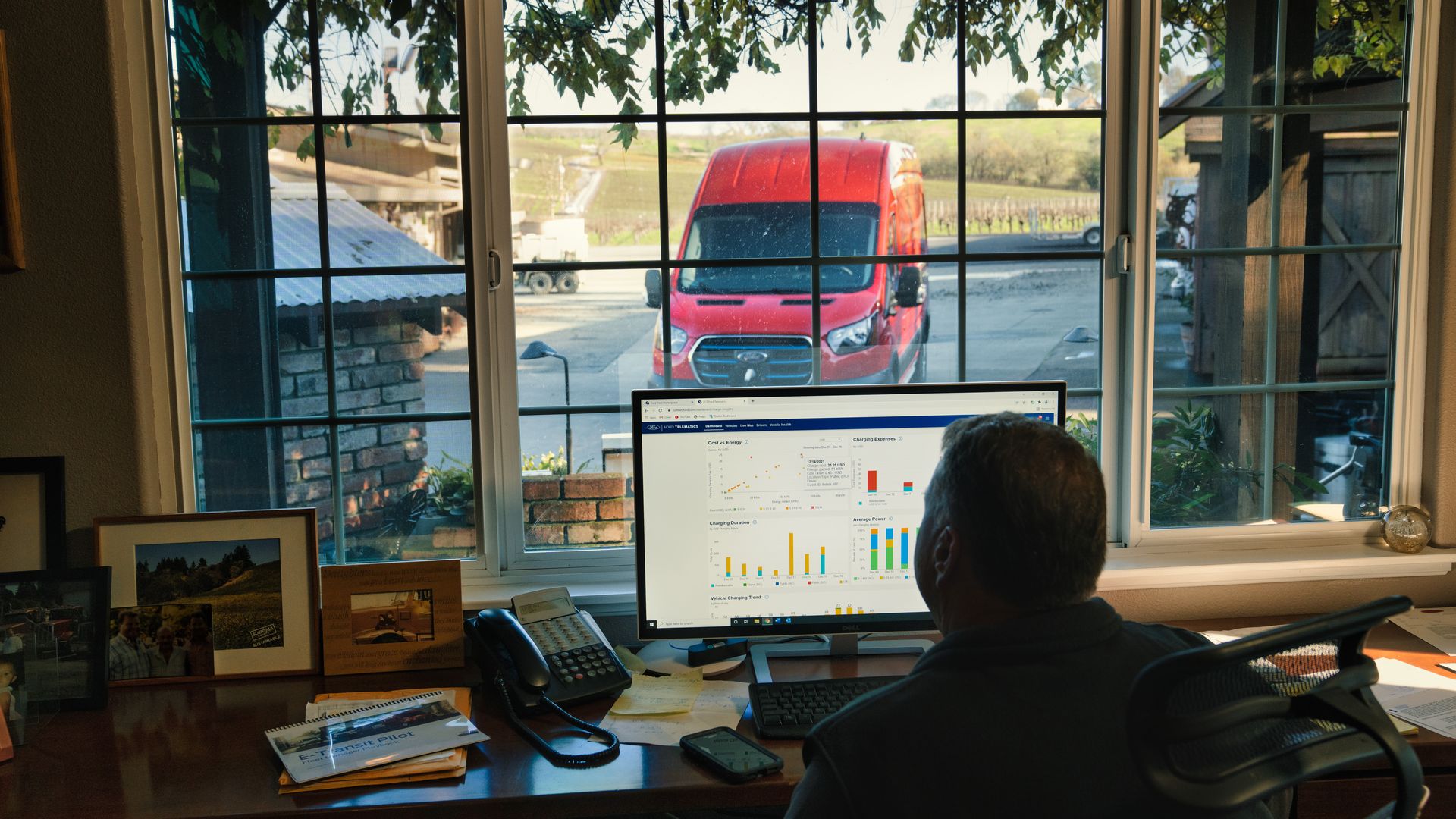 Image of a vineyard owner studying computer data about his connected electric van, parked outside 