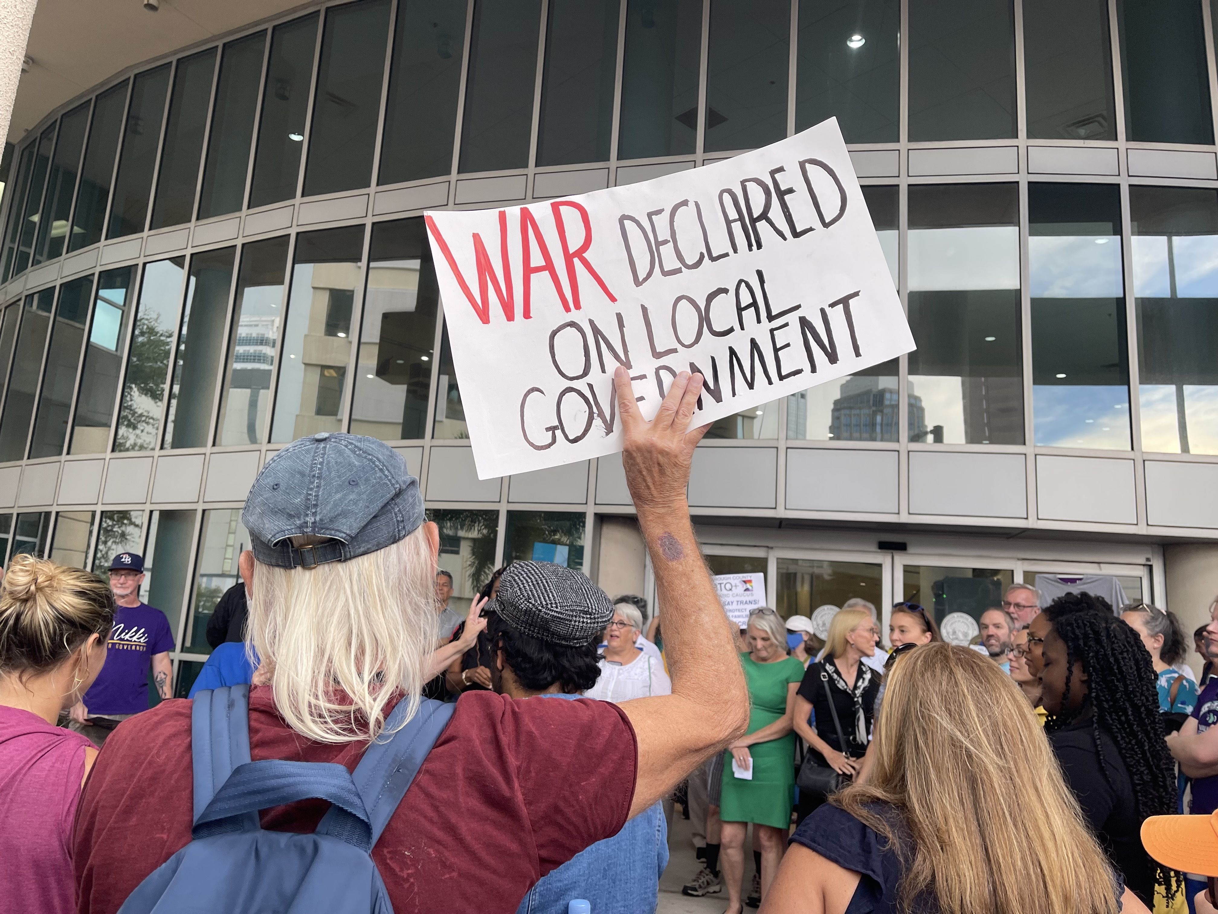 protester holding a sign that says "WAR declared on local government."