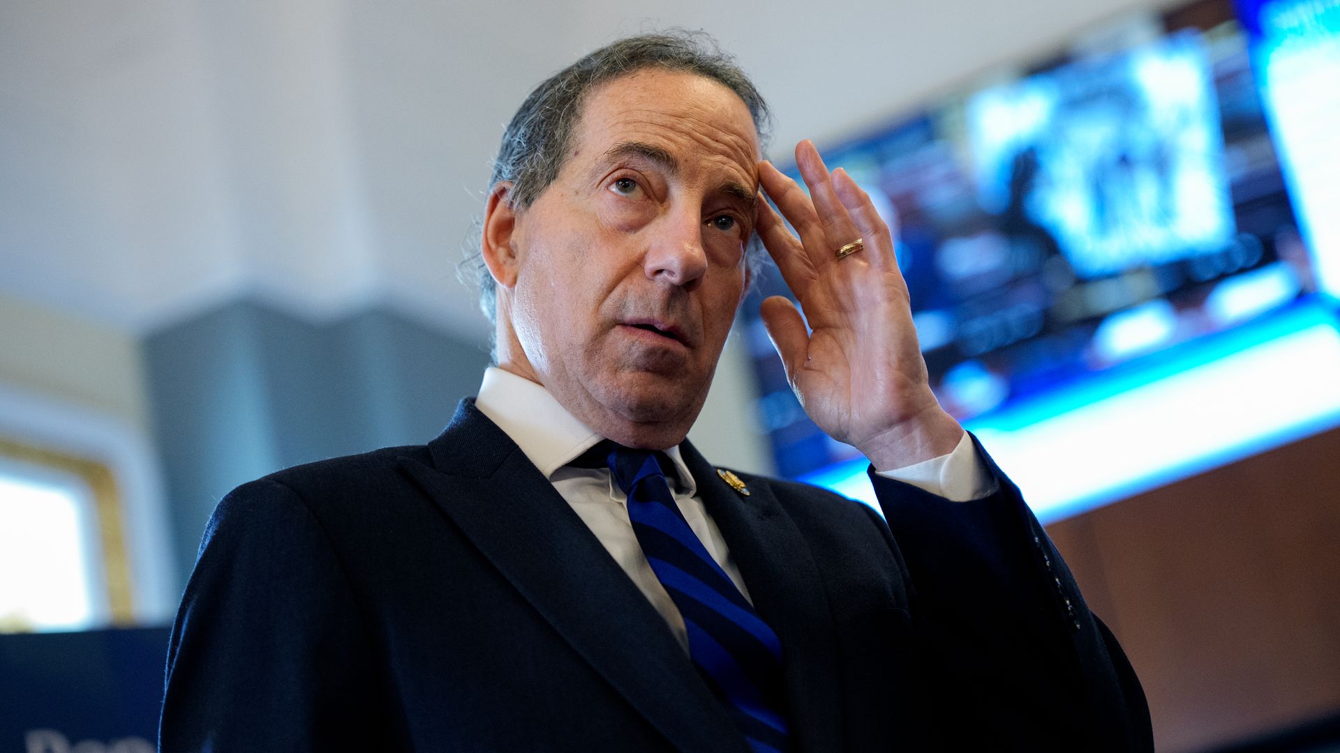 Rep. Jamie Raskin, wearing a black suit and blue tie and pressing a finger to his temple.