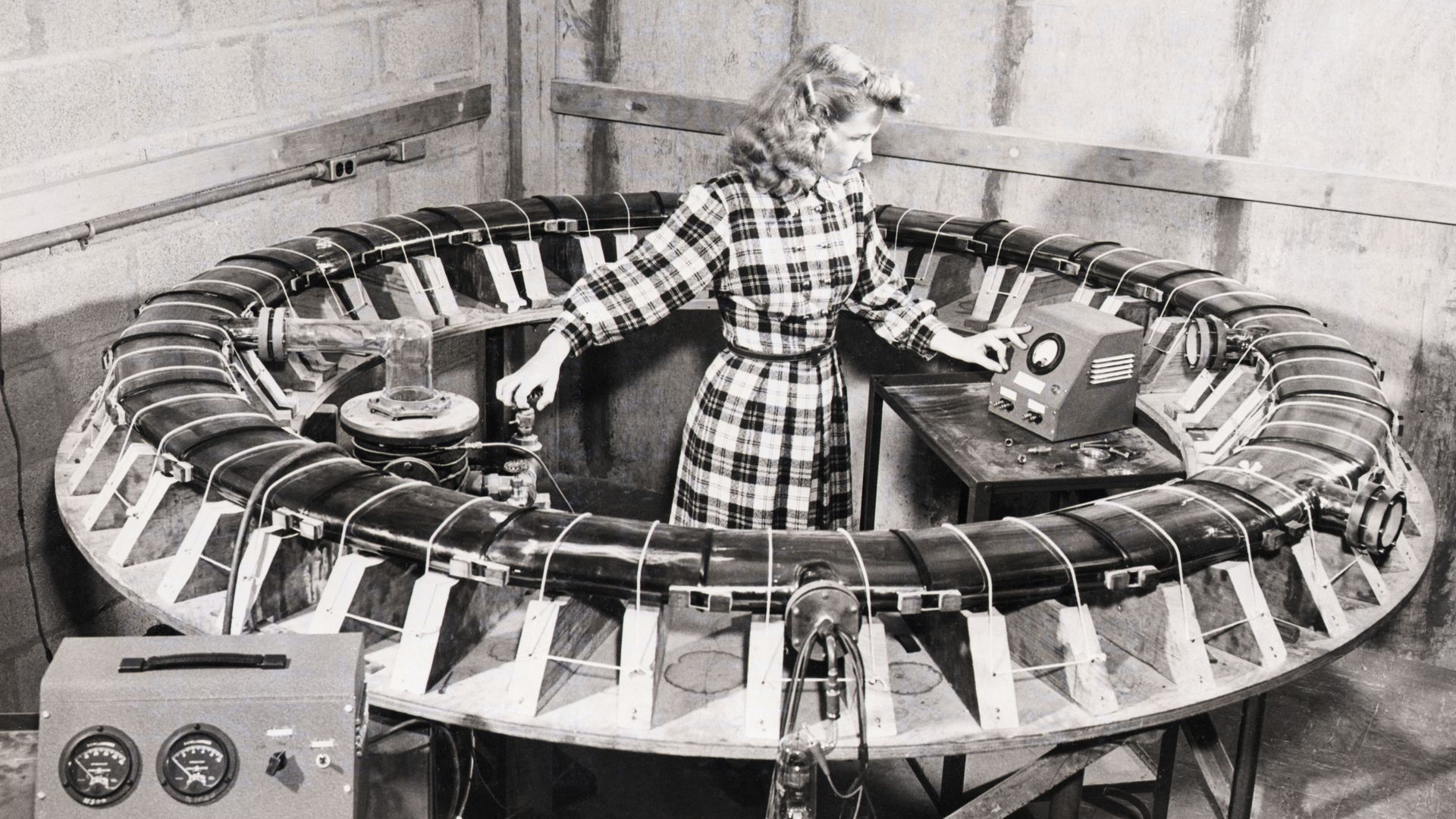 A woman stands inside a circular glass tube for smashing atoms at Cornell Unviersity in 1948