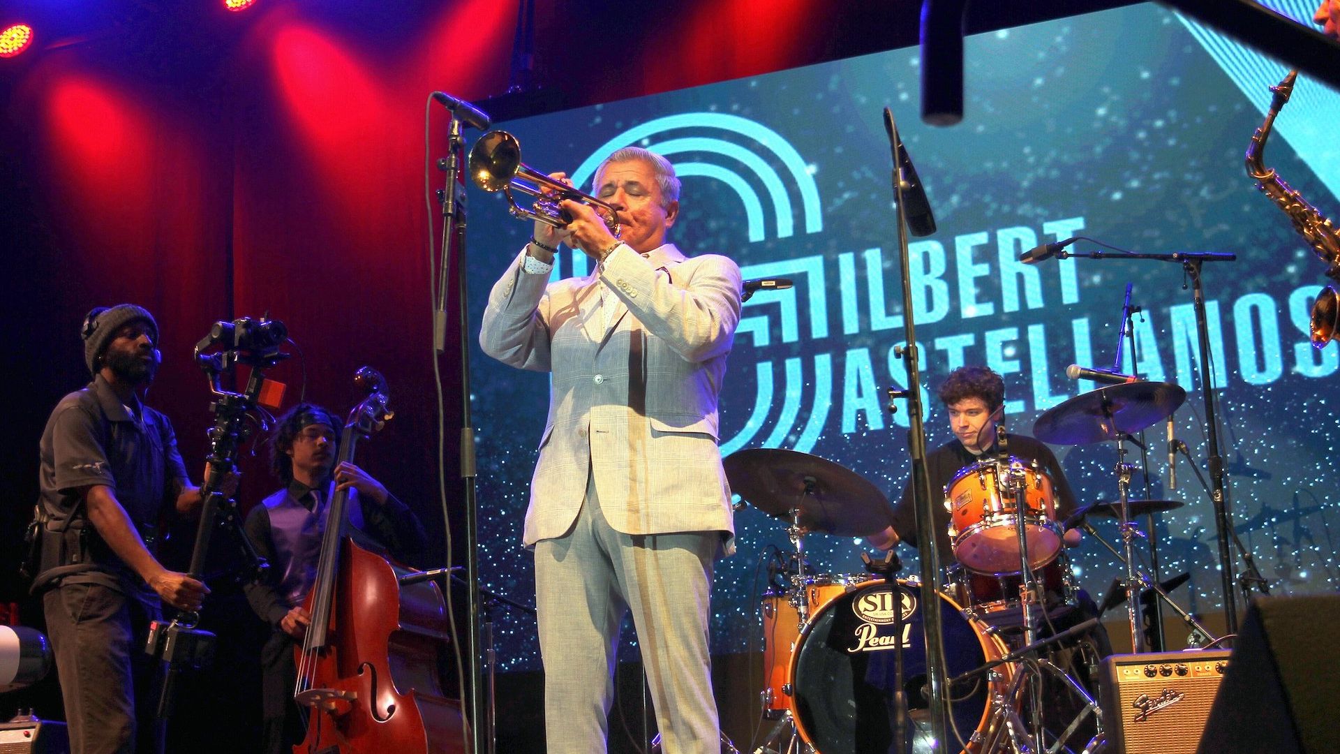 A man plays the trumpet on stage with a band behind him. 