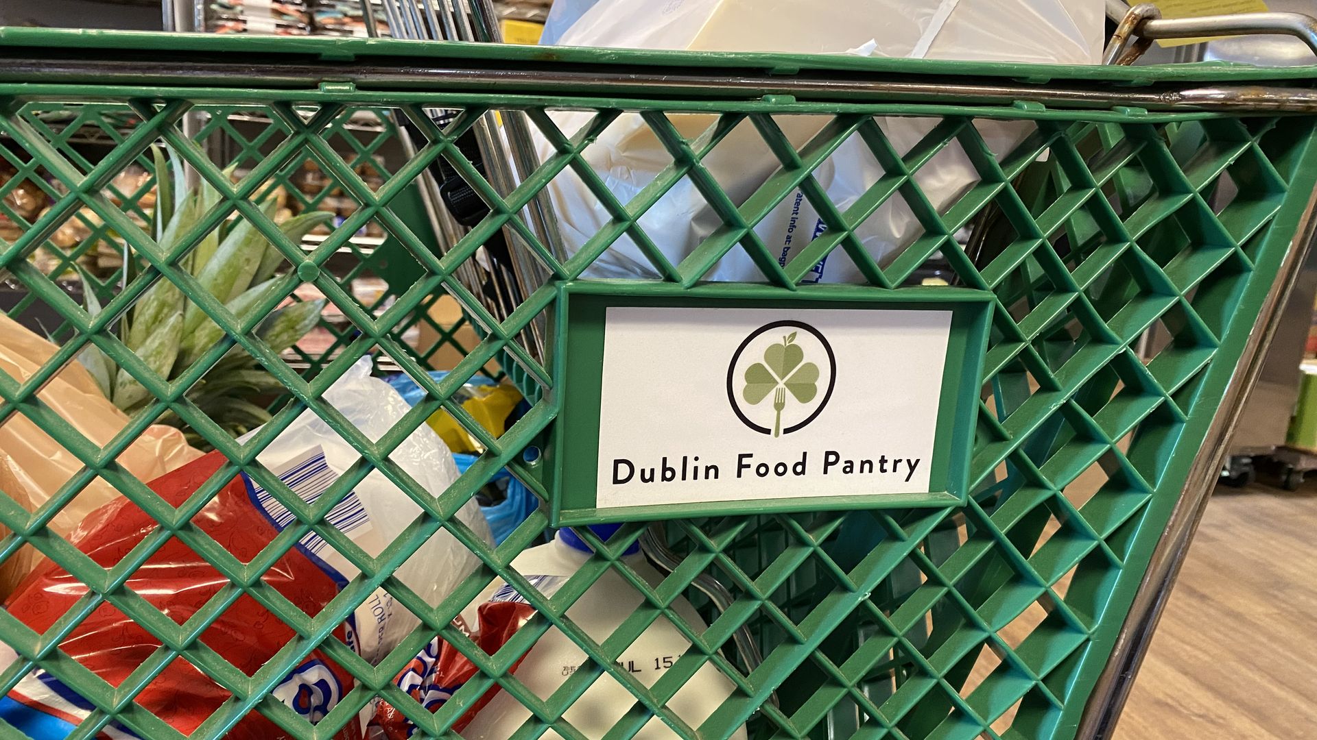 A close-up of a green grocery cart with a Dublin Food Pantry logo