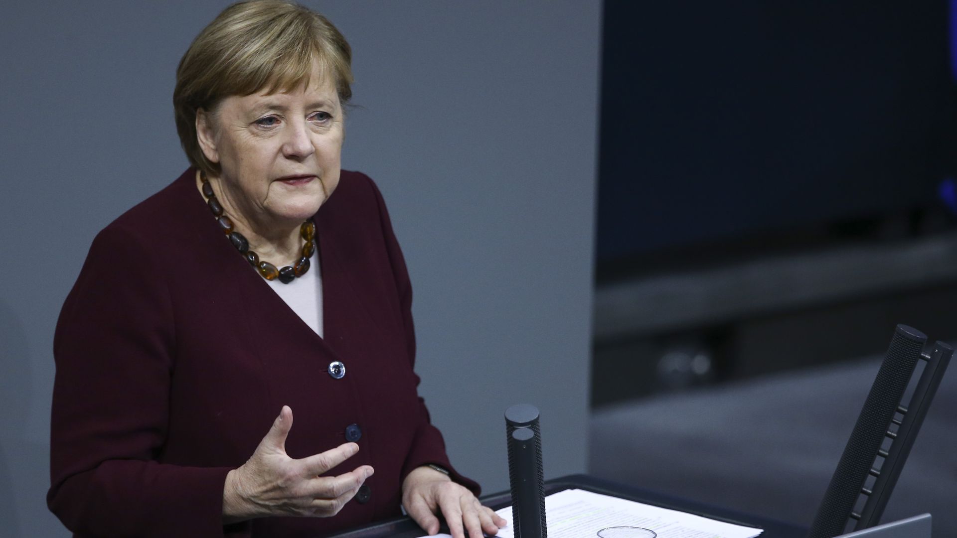German Chancellor Angela Merkel stands in front of an open binder with papers sitting on a podium, while talking and gesturing