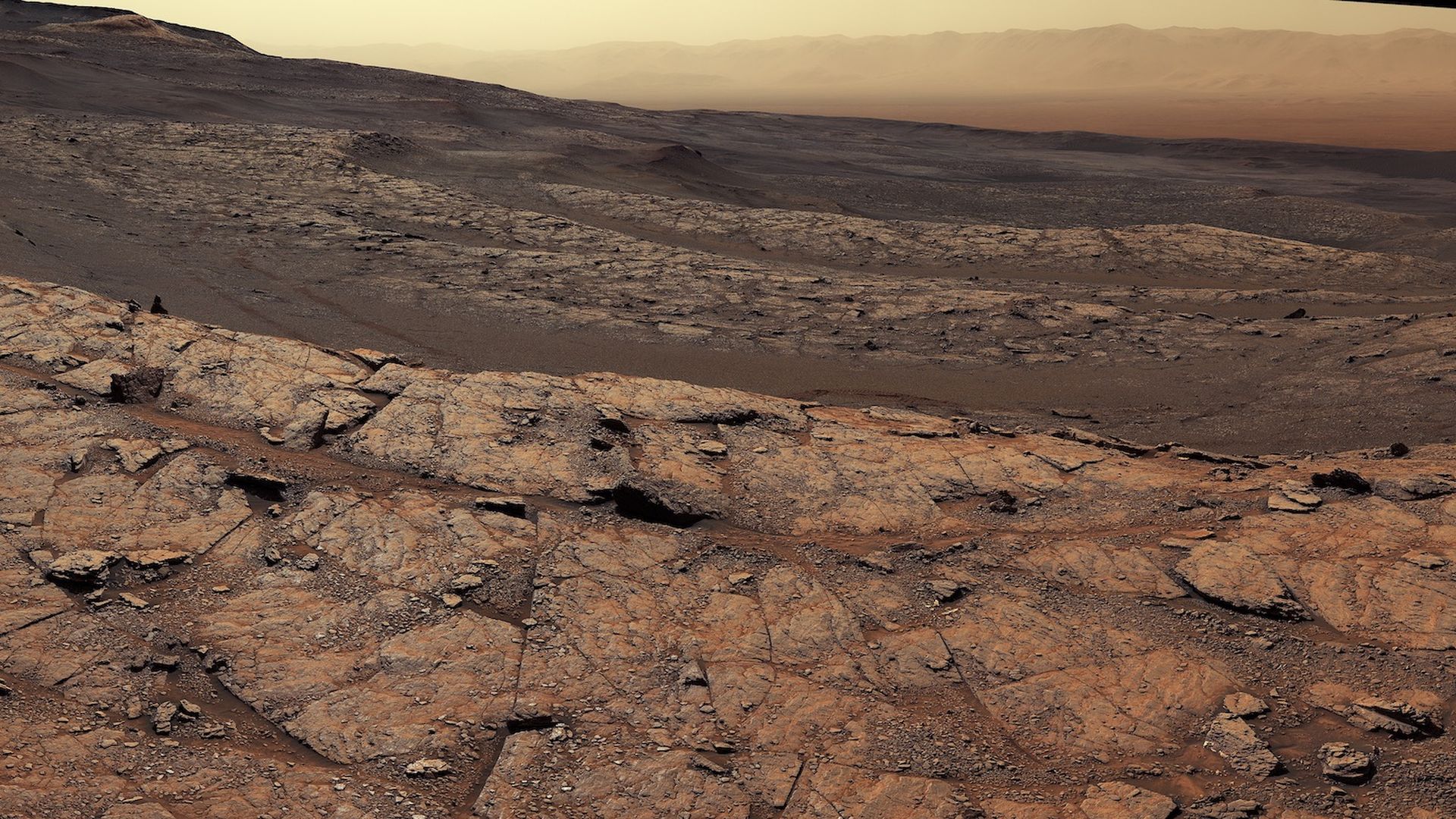 The Martian sky in yellow with mountains in the distance and red dirt below