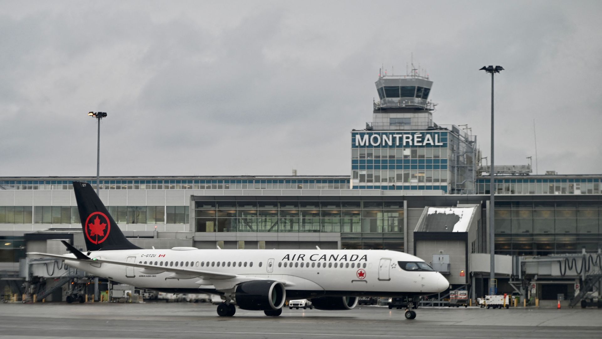 Air Canada jet on tarmac in front of glass building with Montreal on it. Overcast sky. 