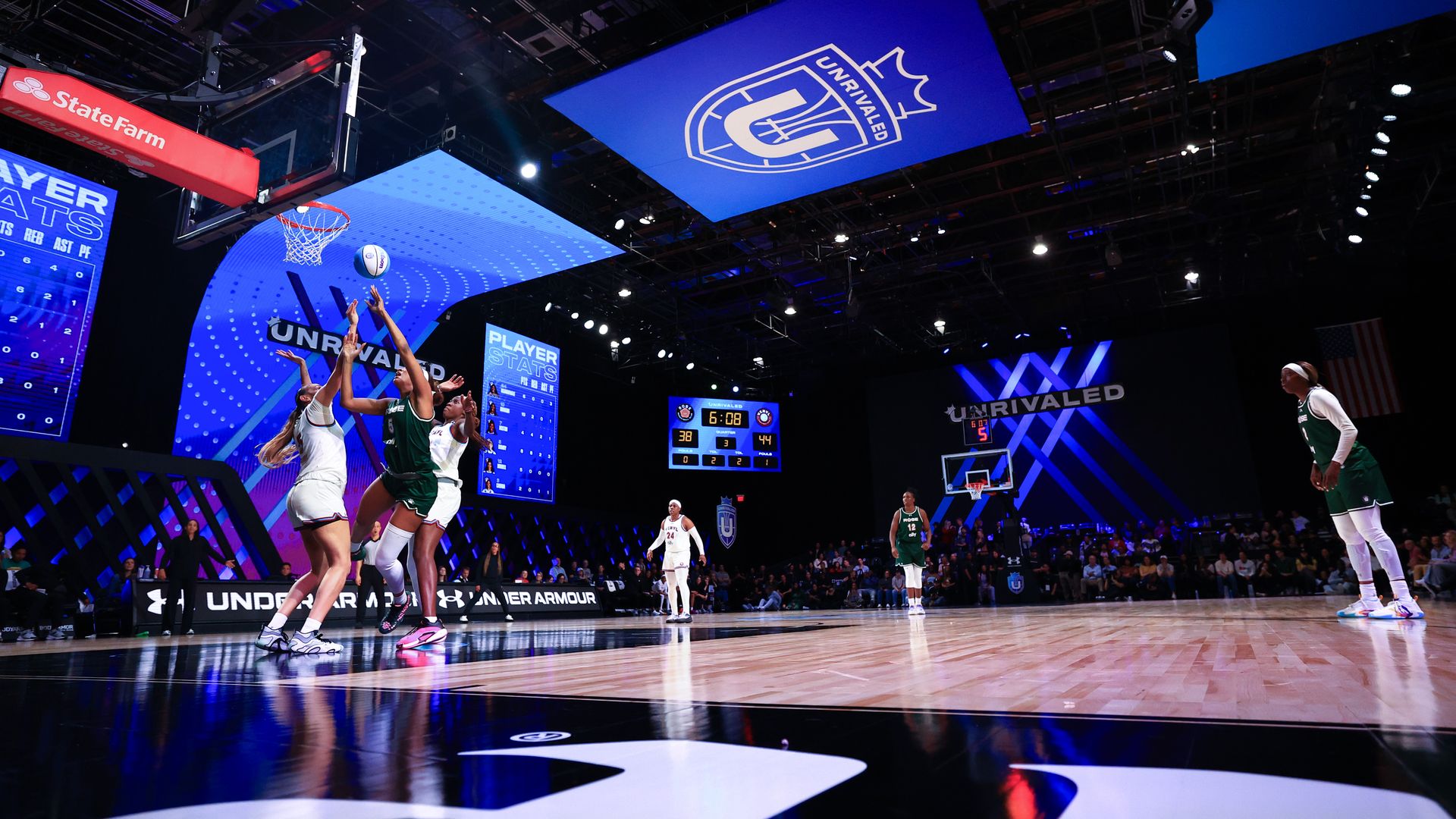 Players battle it out under the basket while others look on. the Unrivaled logo with a shield and crown is visible behind