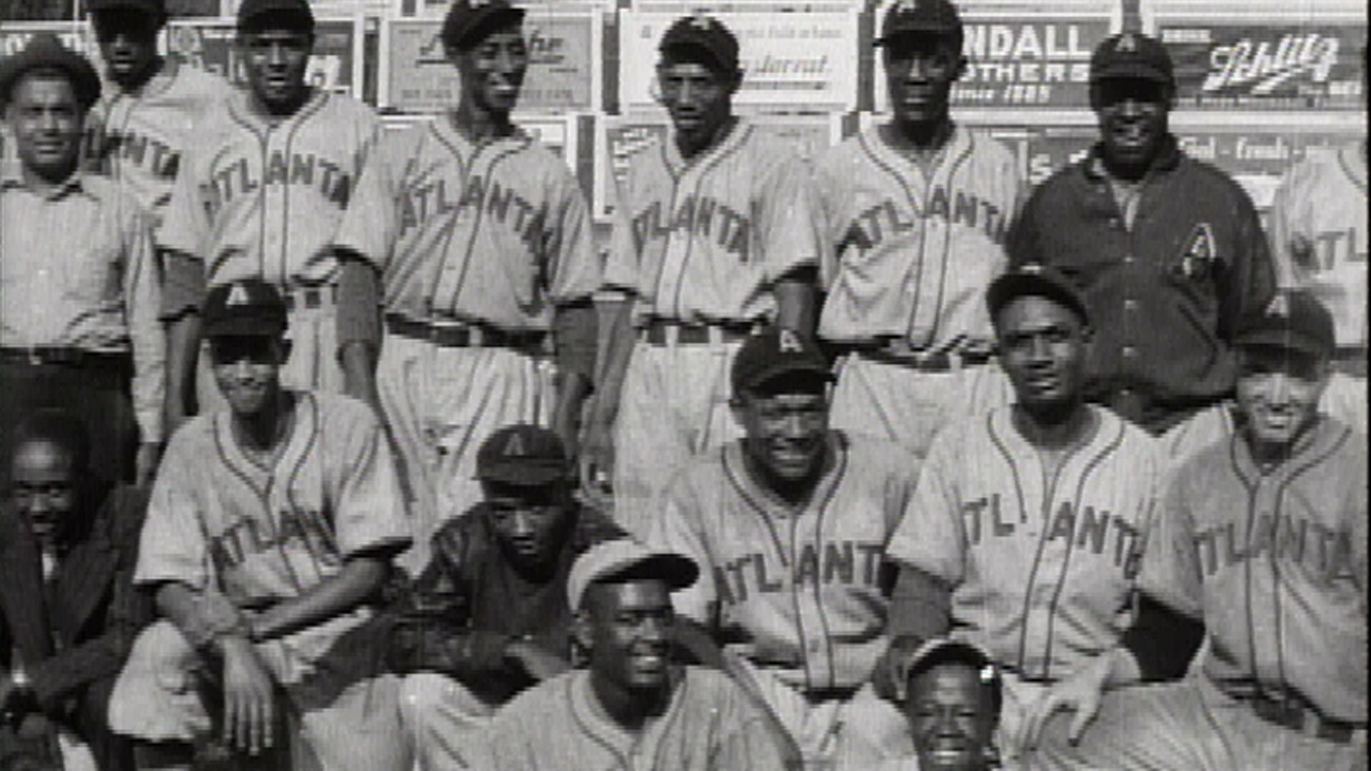 A black-and-white photo of baseball players posing with advertisements in the background