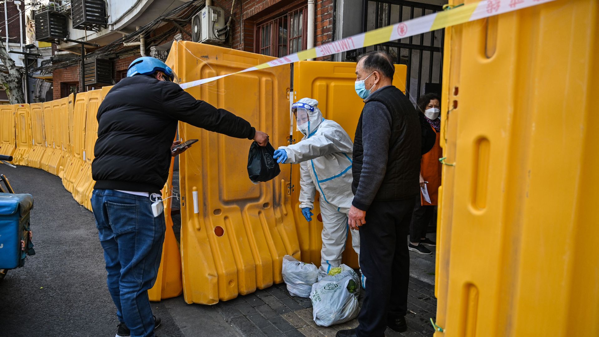 A worker, wearing a protective gear, guards the entrance to a neighborhood in lockdown as a measure against the Covid-19 coronavirus receive food from a delivery man.