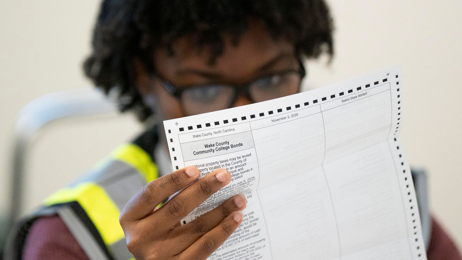 Mail-in ballots are prepared at the Wake County Board of Elections in Raleigh. A woman wearing a neon and gray vest peers through glasses at a folded ballot.