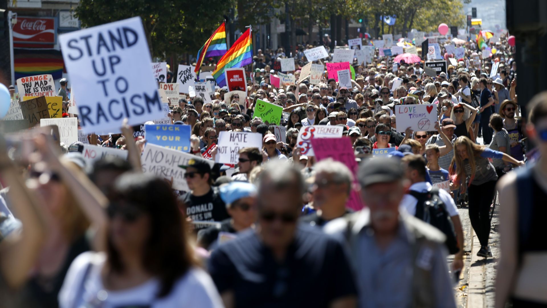 Photo of a crowd of people marching down the streets with Pride flags and "Stand up to racism" signs