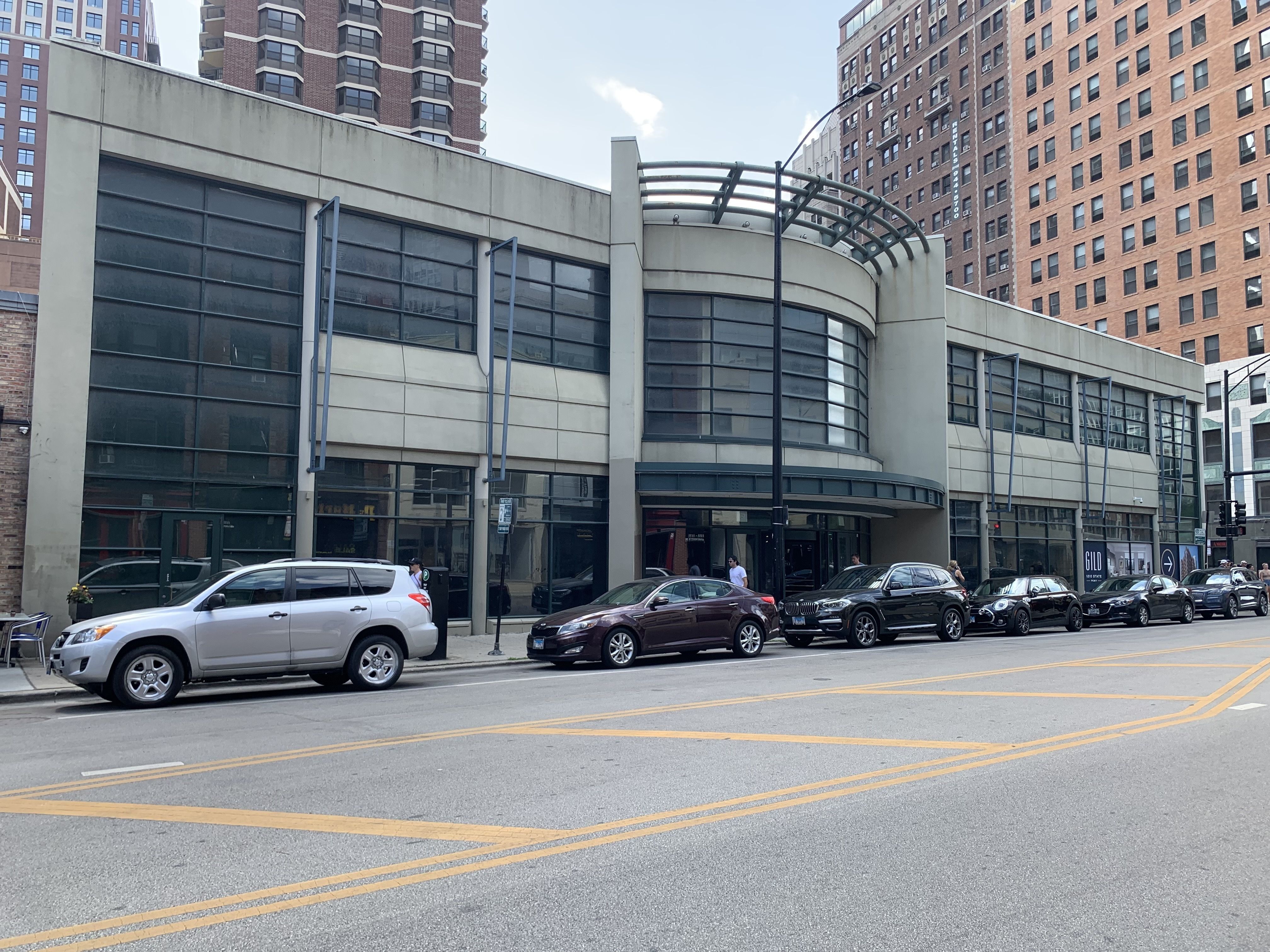 Empty building with cars parked out front in a row on the street.