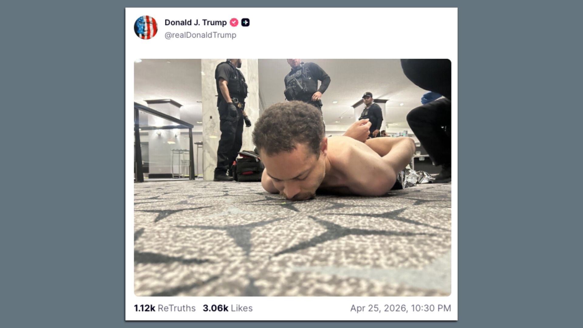 Shirtless man lying face down on a patterned carpet inside a public indoor space, surrounded by several armed officers in tactical gear