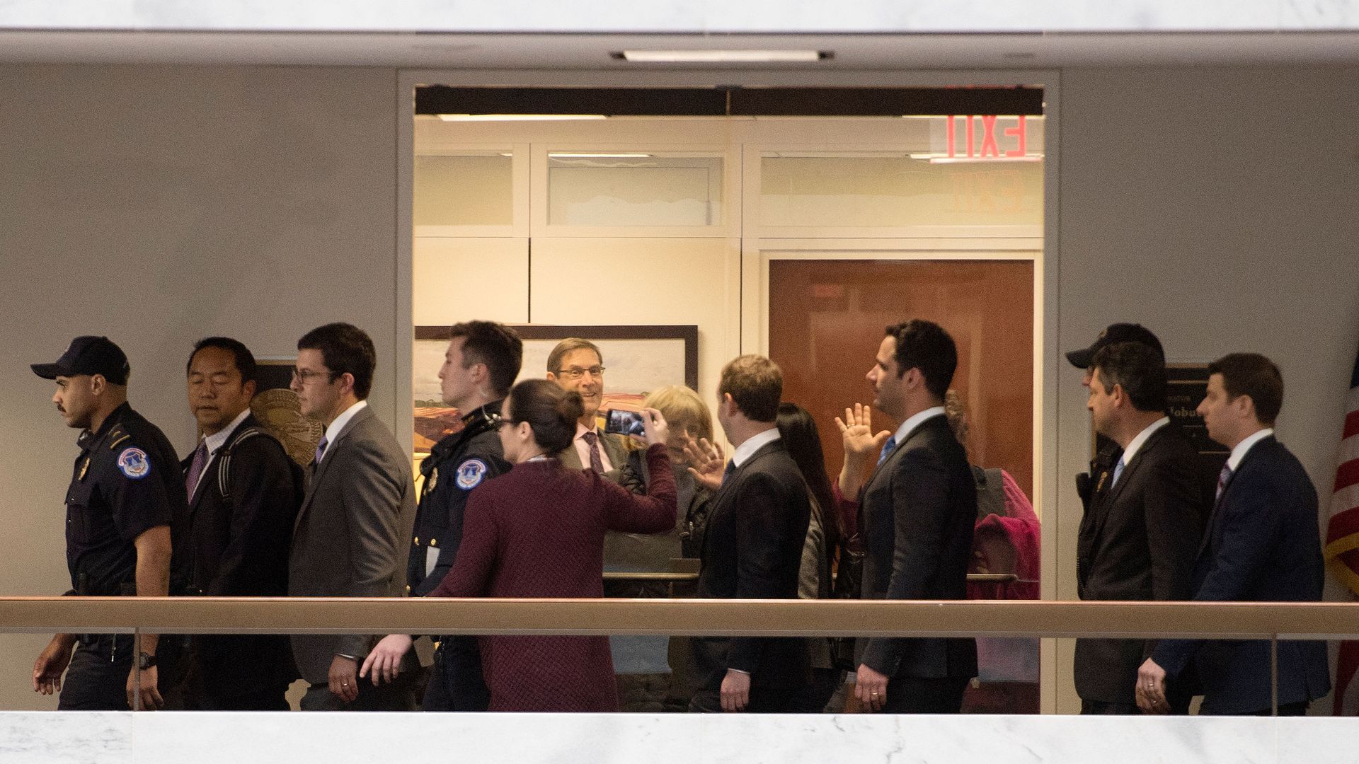 Staffers wave through a glass door at Mark Zuckerberg as he walks by