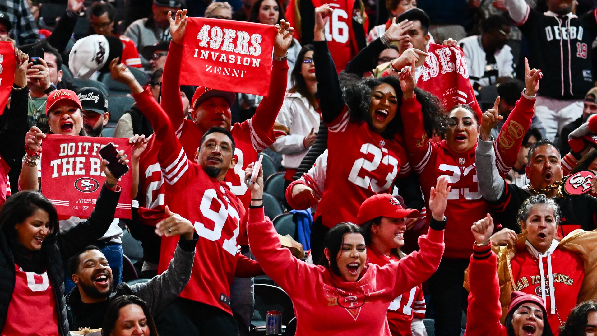 Cheering crowd of Niners fans in Niners gear. One fan holding up sign that says "49ers invasion"