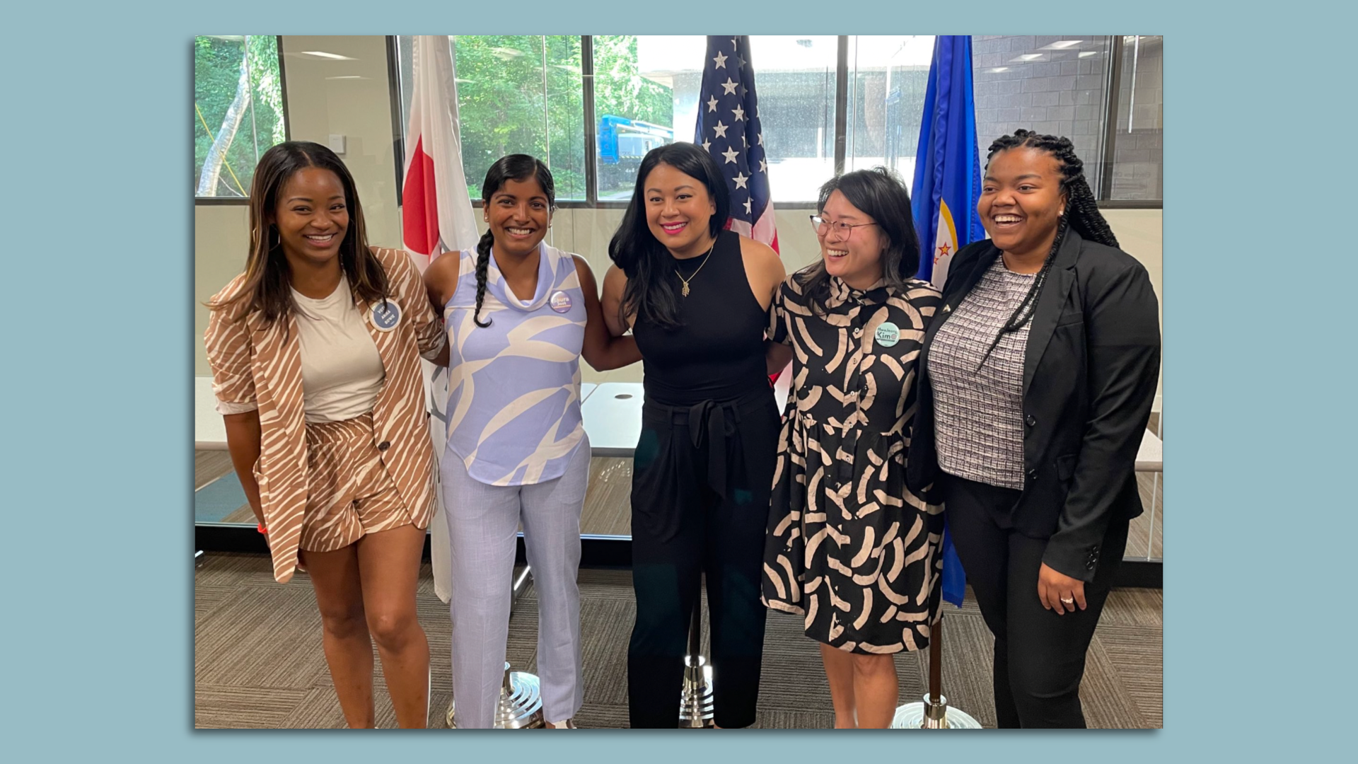 Five women stand together in front of flags 