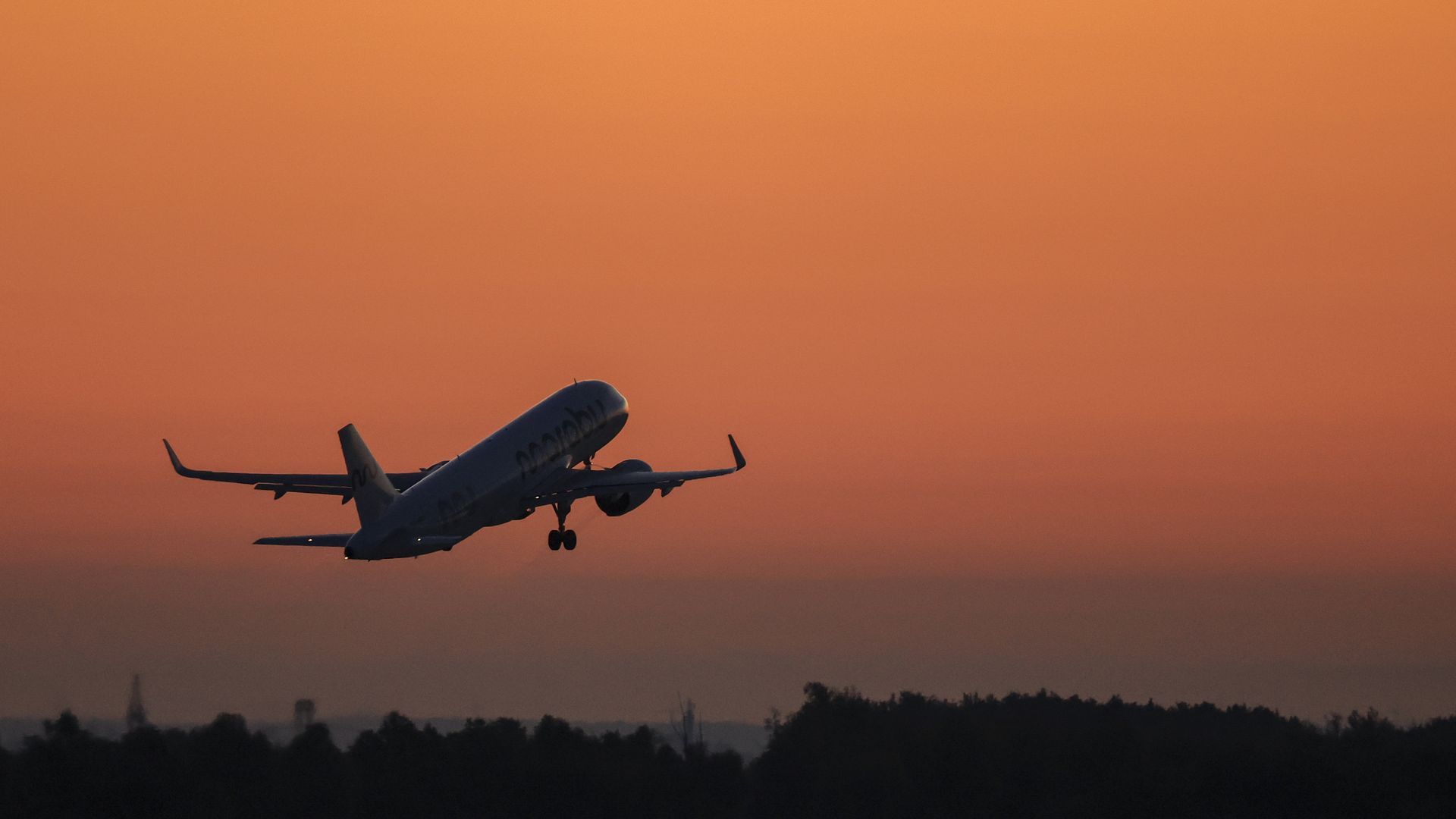 A commercial plane flies with a sunset in the background. 