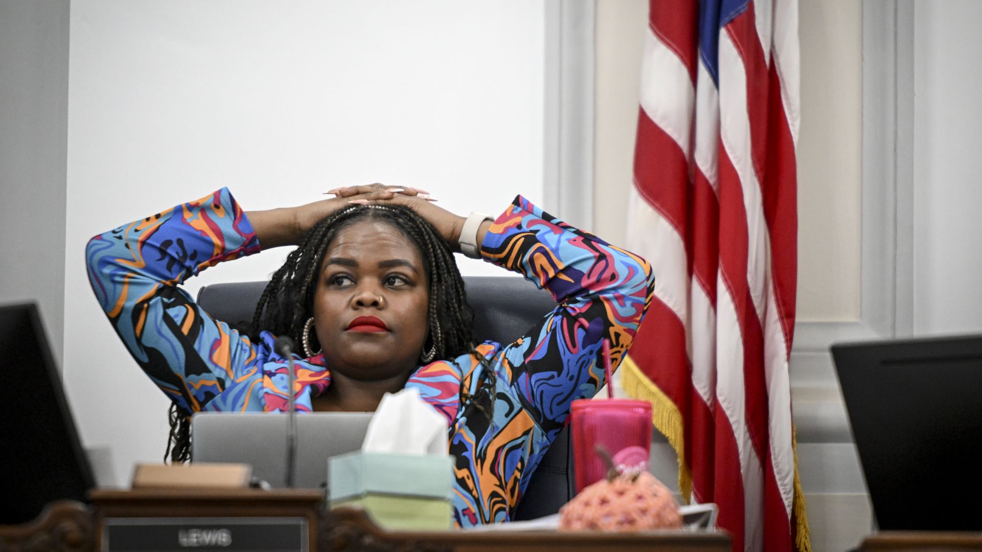 A woman with a colorful jacket places her hands over her head while appearing concerned. 