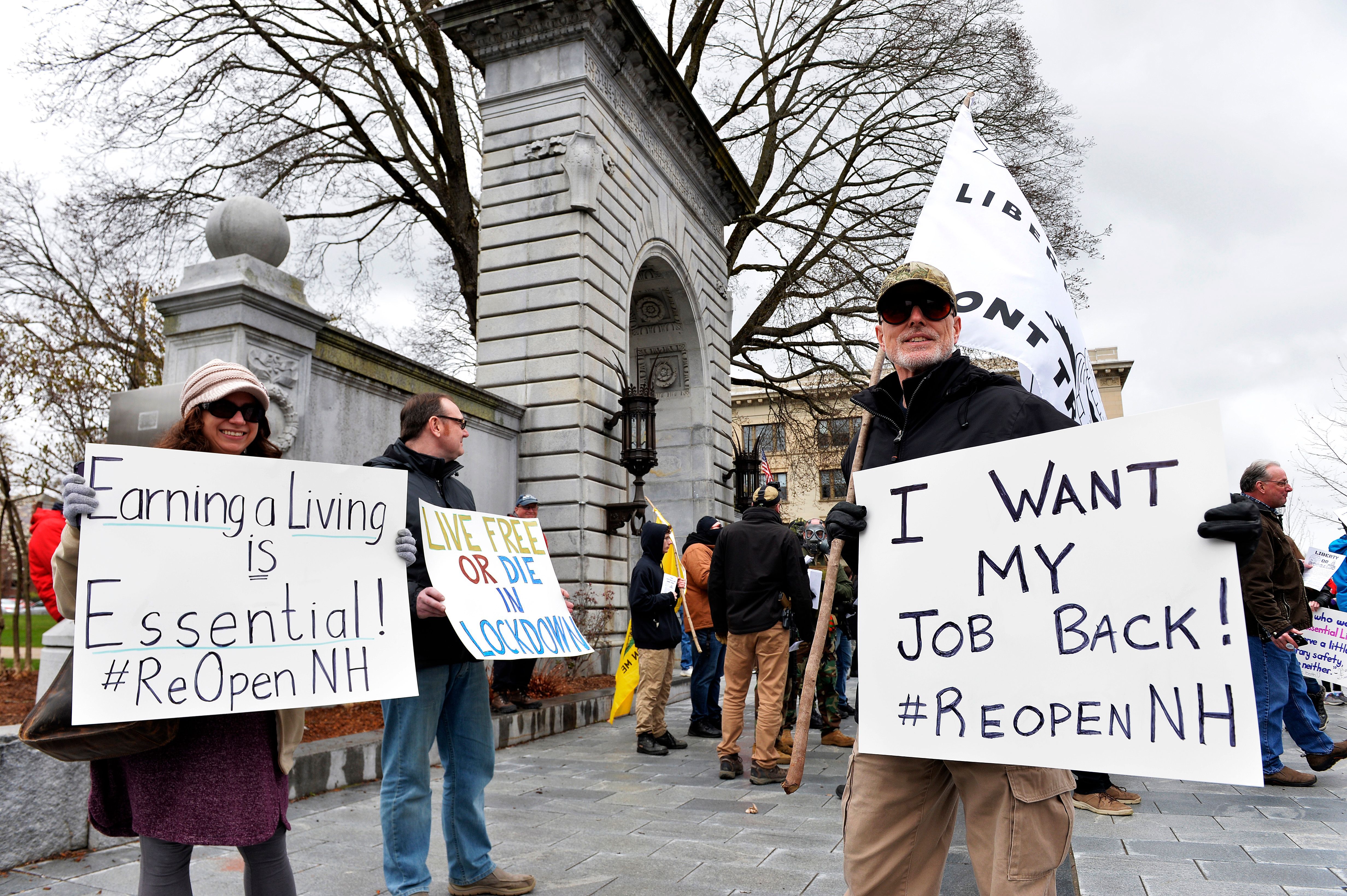 In this image, a woman holds a sign that reads "earning a living is essential" and a man holds a sign that reads "i want my job back"