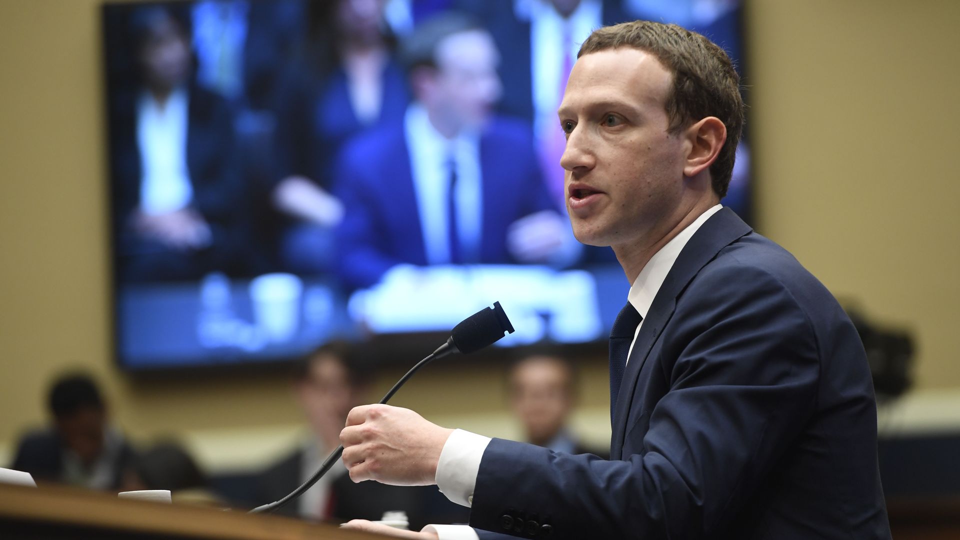 Mark Zuckerberg testifying in front of a big-screen TV that also shows him testifying