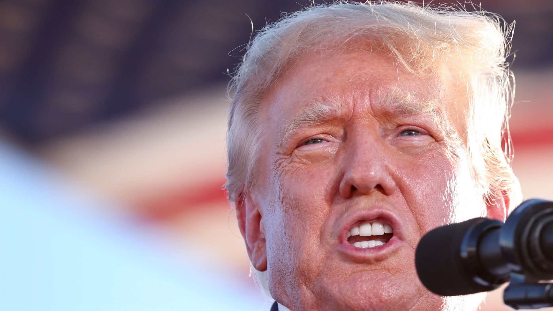 Former President Donald Trump, wearing a blue suit and white shirt with no tie, speaks at the podium at a rally in Arizona.