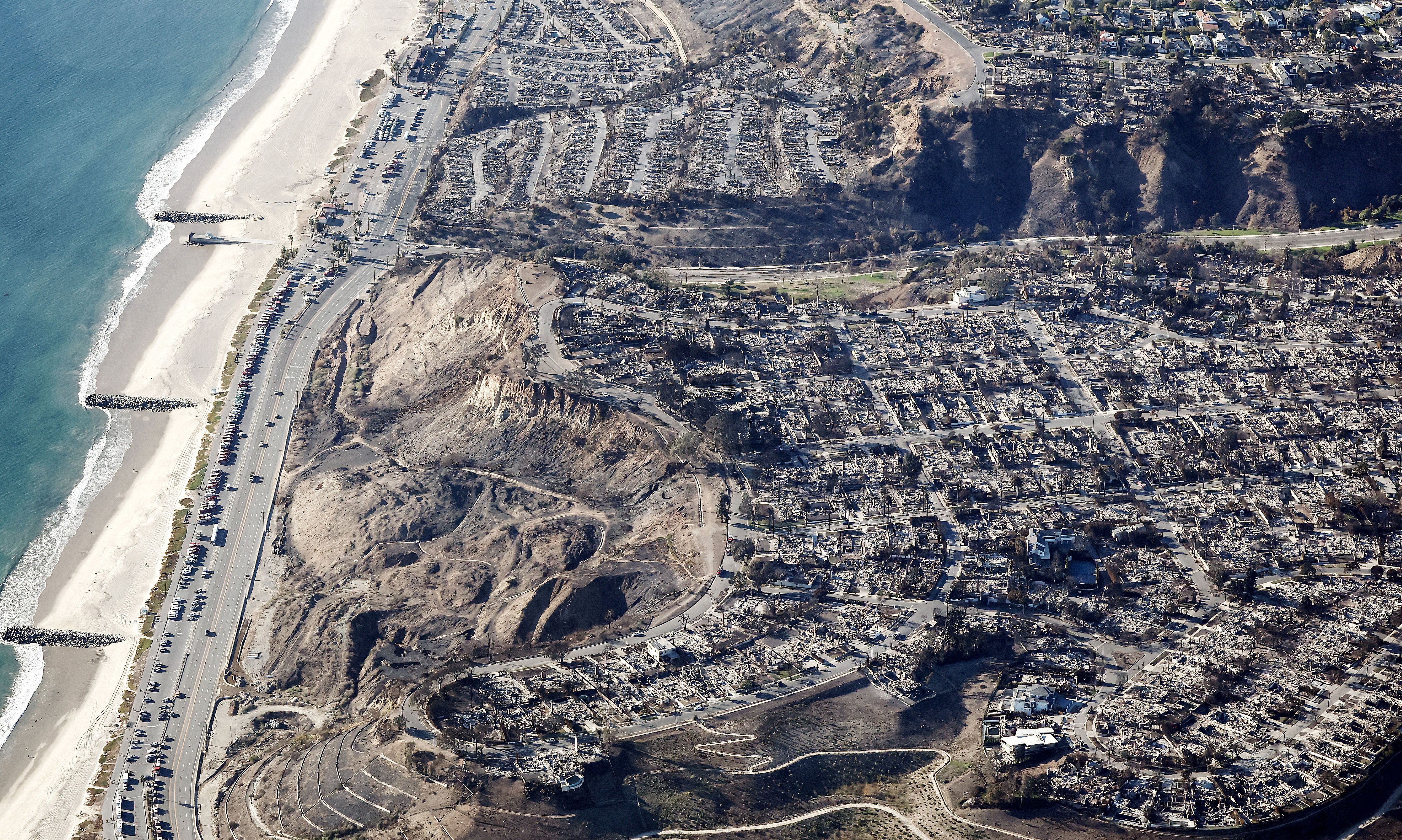  fire trucks, utility, and other vehicles parked along Pacific Coast Highway near homes destroyed in the Palisades Fire as wildfires cause damage and loss through the LA region on January 13, 2025 in Pacific Palisades, California. Multiple wildfires fueled by intense Santa Ana Winds continue to burn