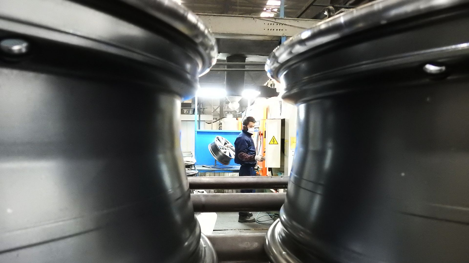 In this image, a Chinese worker inspects wheel hubs at a factory. 