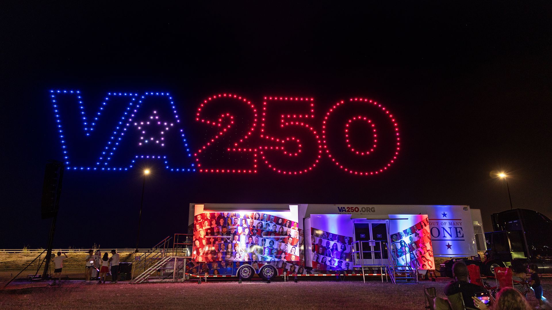 Night scene of a large blue-and-red LED sign reading VA250, with a blue VA and star motif and red 250. A colorful photo-mosaic trailer sits below at an outdoor event.