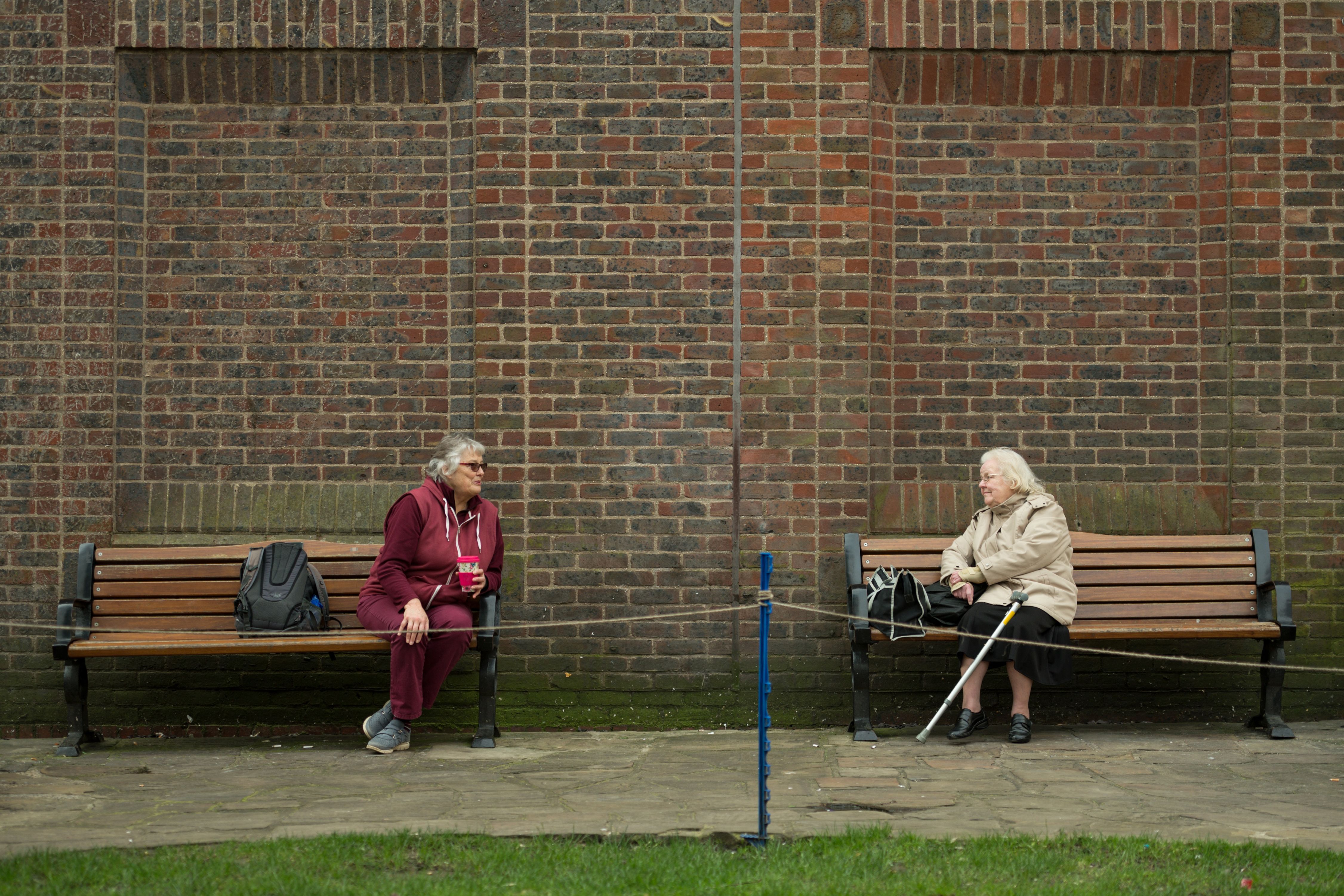  Two women observe social distancing measures as they speak to each other from adjacent park benches amidst the novel coronavirus COVID-19 pandemic, in the centre of York, northern England on March 19