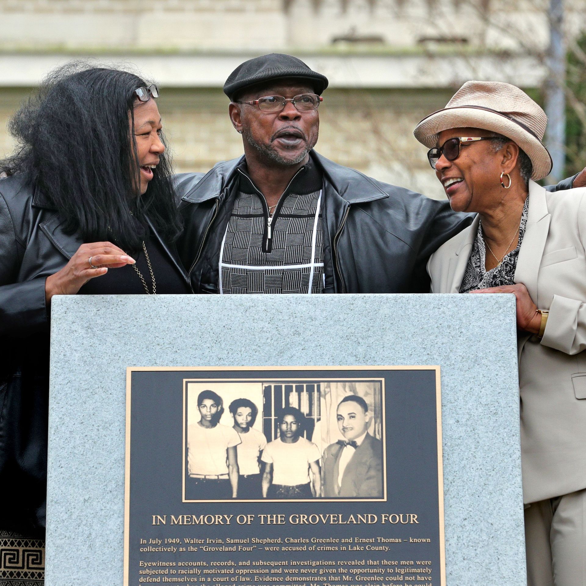 A man and two woman stand behind a granite monument with a plaque that reads "In Memory of the Groveland Four" under an image of four young men.  