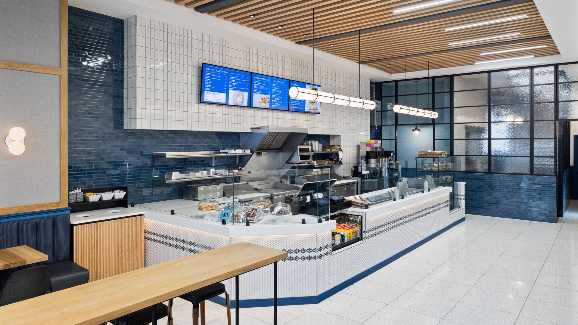 The interior of H&H Bagels new location on the Upper West Side, which includes a long counter with white tiled walls and floor.