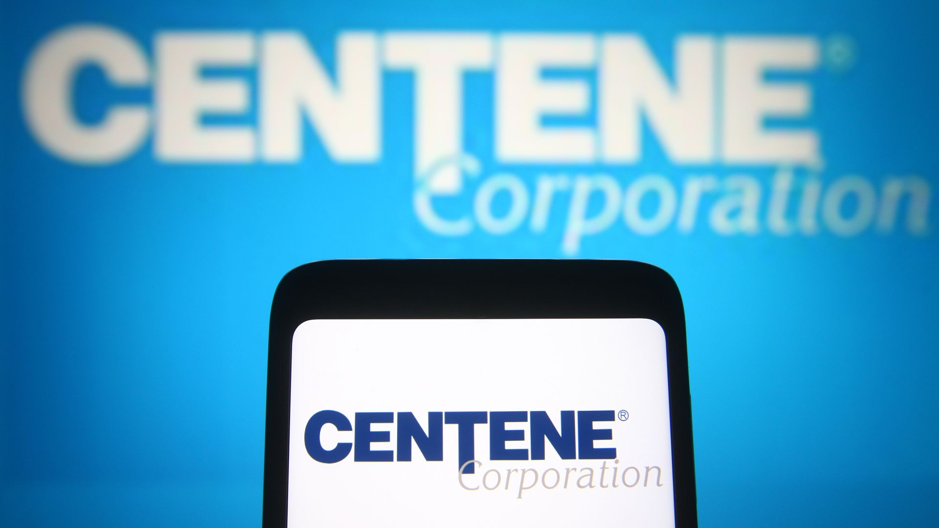 The blue Centene logo on a phone, in front of a blue background and white Centene logo.