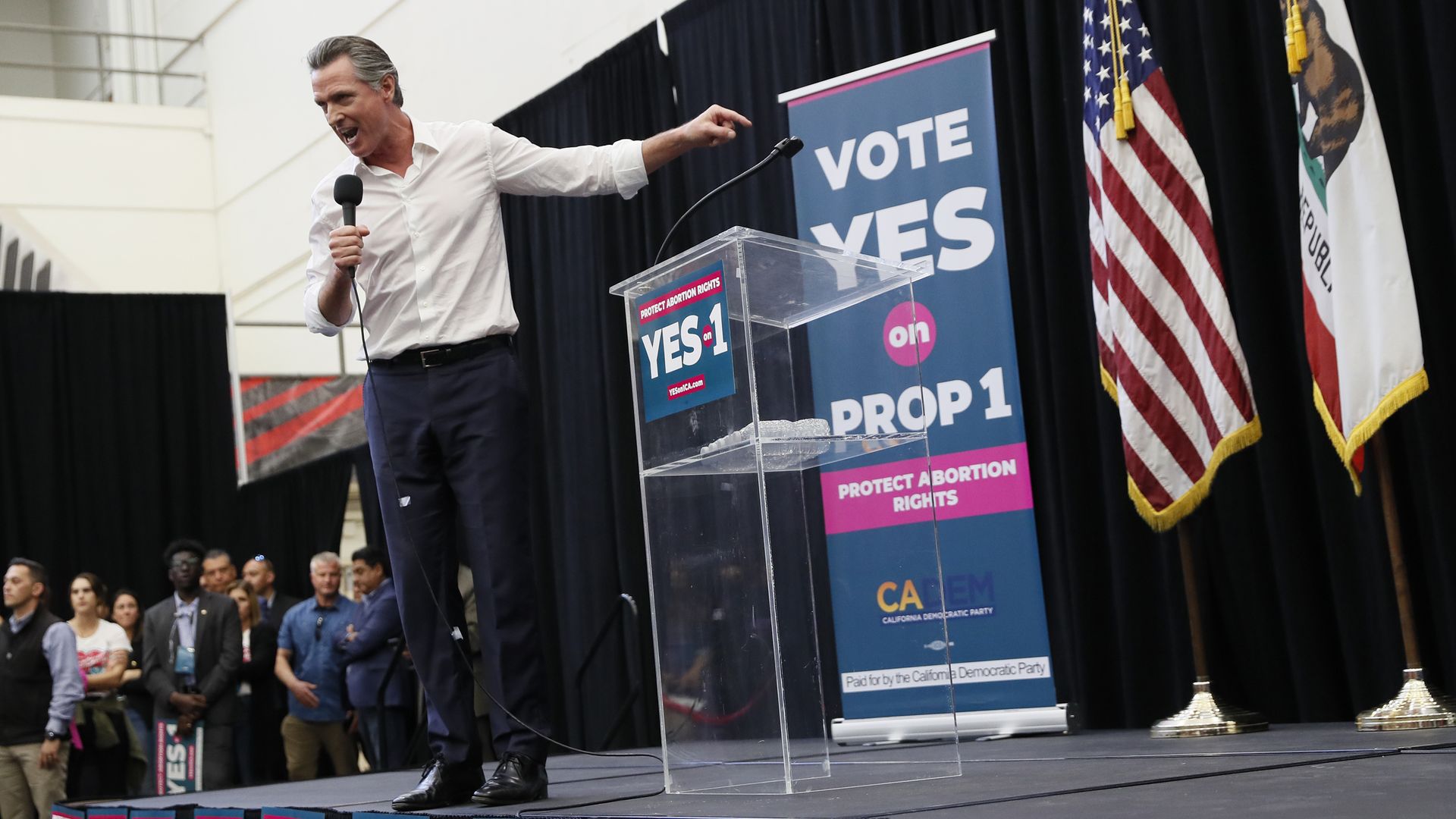 Picture of Gavin Newsom on a stage surrounded by signs that say "Vote Yes on Prop 1"