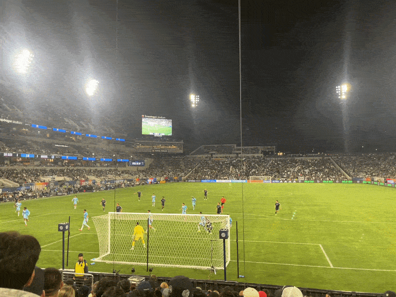 A GIF of San Diego FC soccer player scoring a goal off of a cross. Fans jump up in excitement and blue fireworks go off behind the goal. 