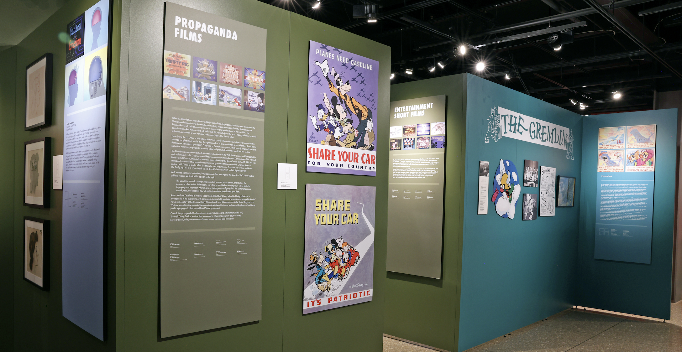 Exhibit on propaganda films in a museum: green walls with large panels and posters, plus a teal wall featuring "The Gremlin" cartoons.
