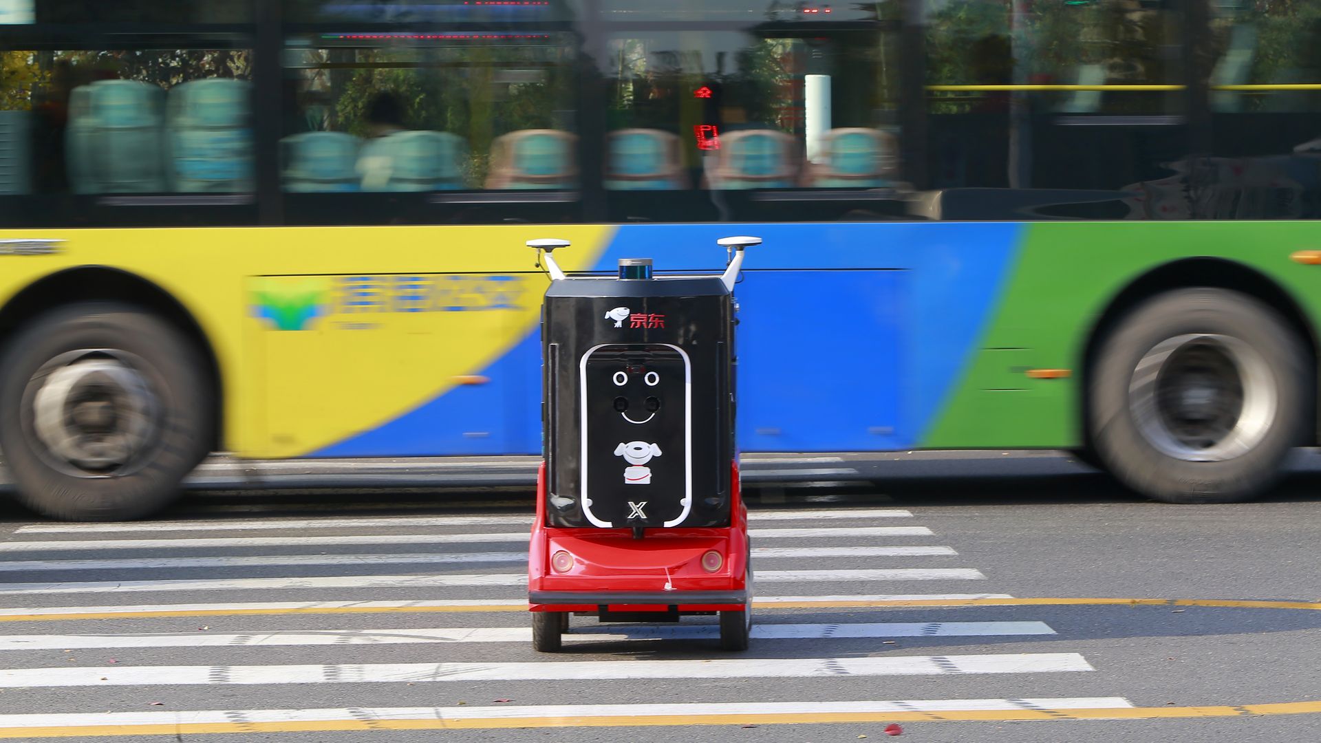 A red and black robot with a smiley face rolls across the street