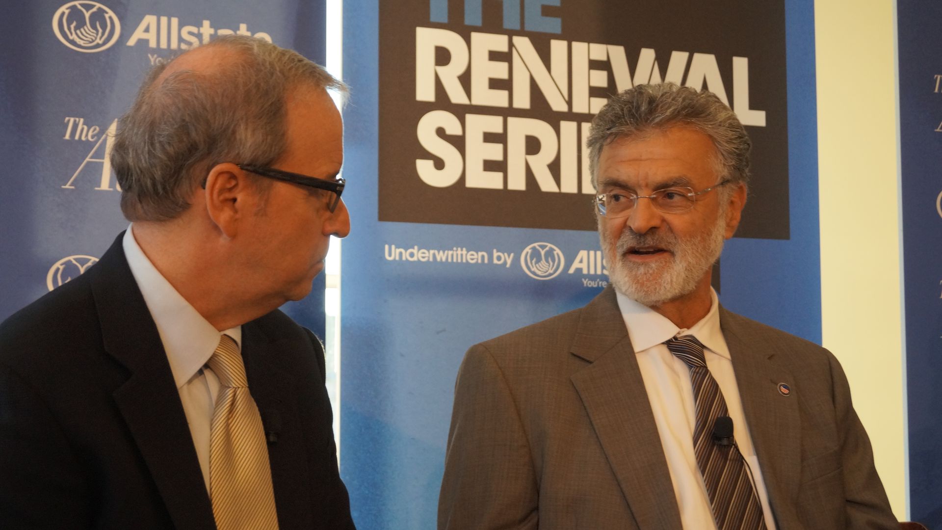 Cleveland Mayor Frank Jackson, in suit and tie, in conversation with man in glasses. Blue background. 