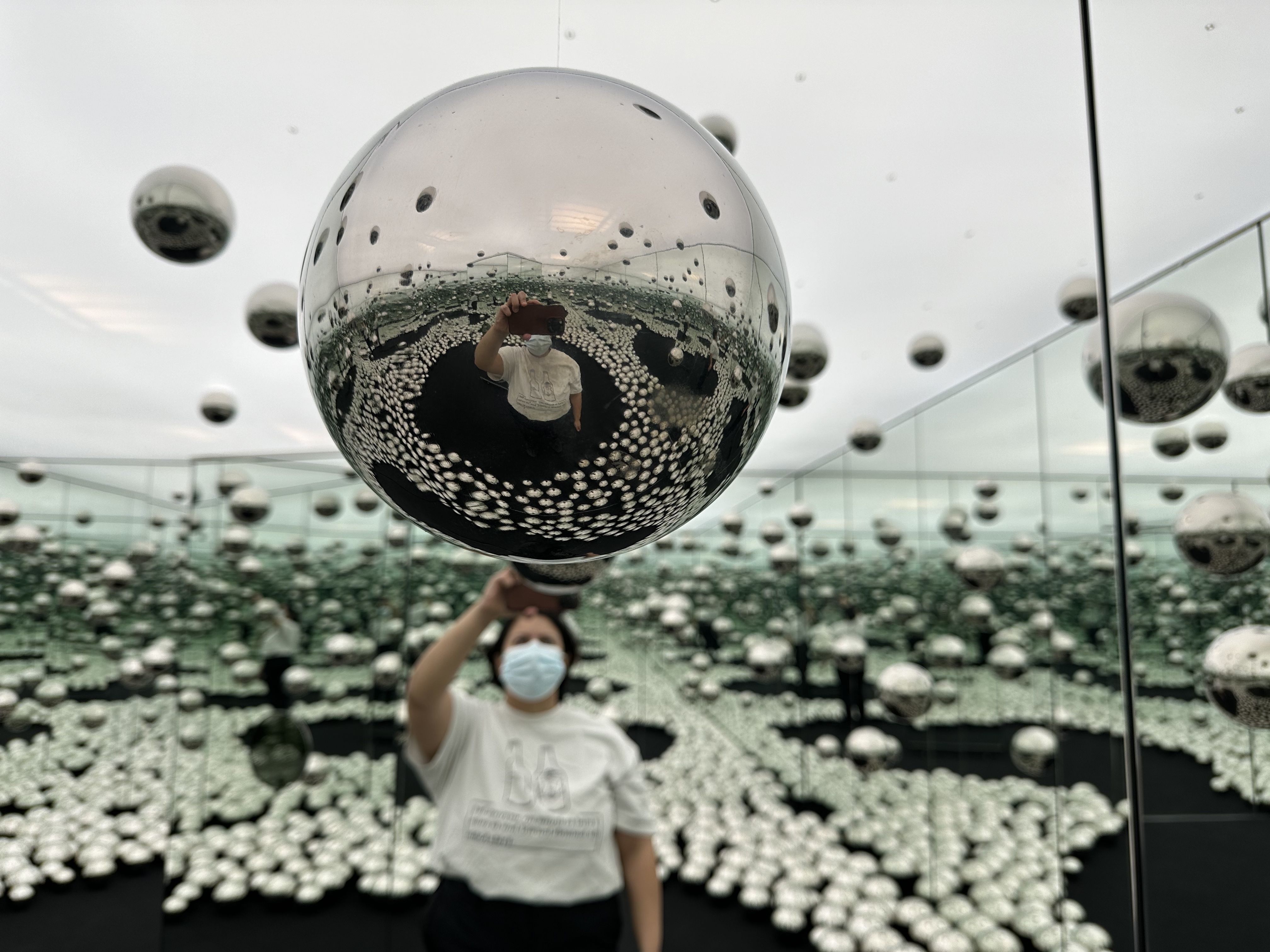A reporter takes a photograph of a stainless steel ball in a mirrored room filled with them as part of Yayoi Kusama's "Let's Survive Forever" installation, seen at the WNDR Museum in Boston.