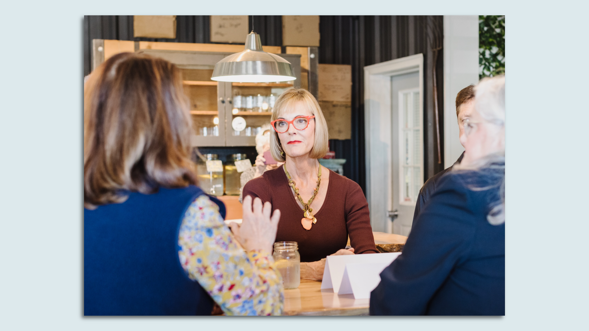 A woman in red glasses sits across a table from two others. 