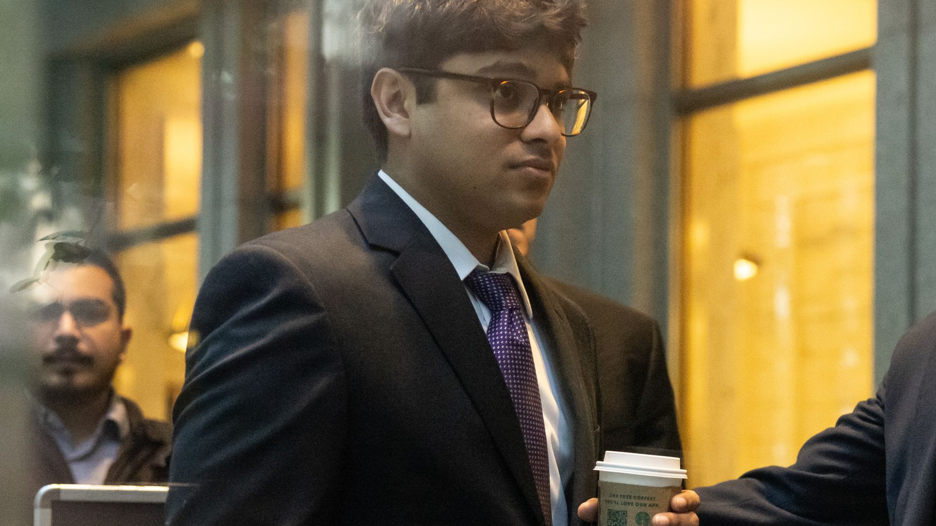A young man, in a suit, seen through glass.