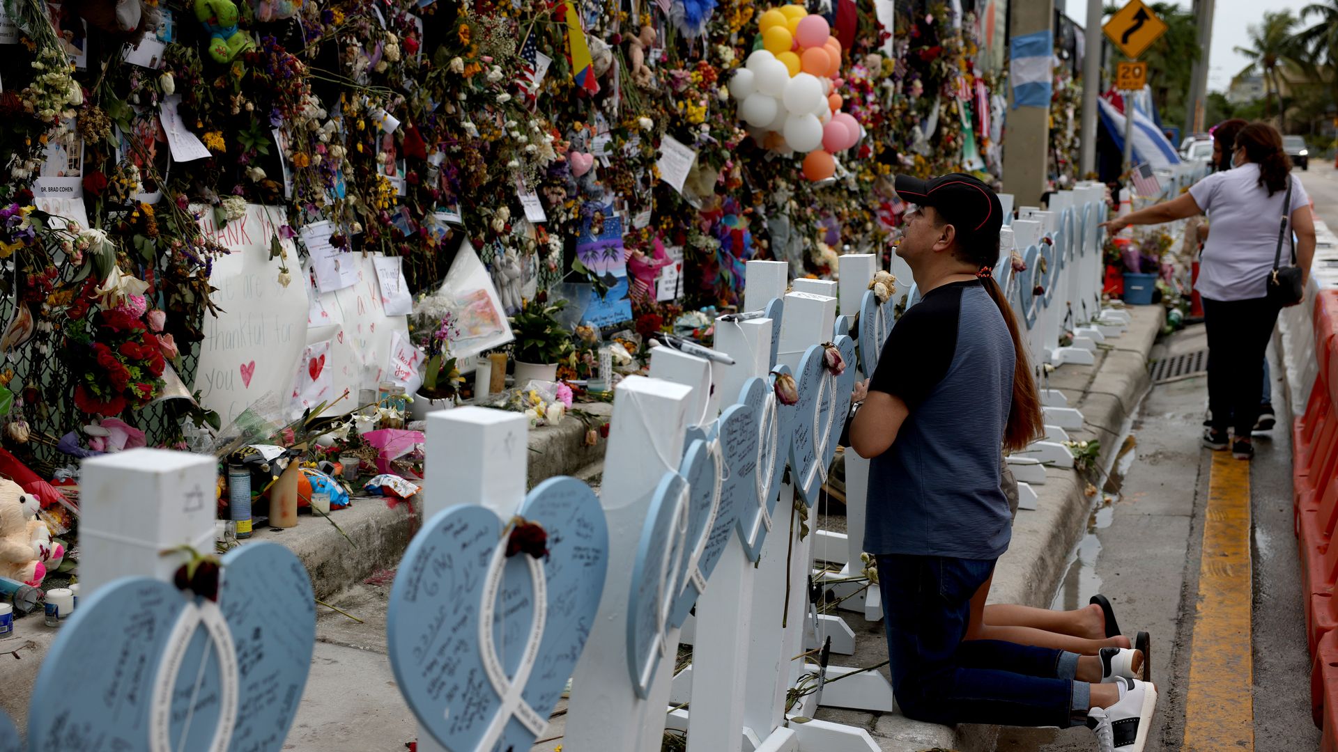 Photo of people kneeling and praying at a memorial filled with flowers and plushies for victims of the Surfside collapse