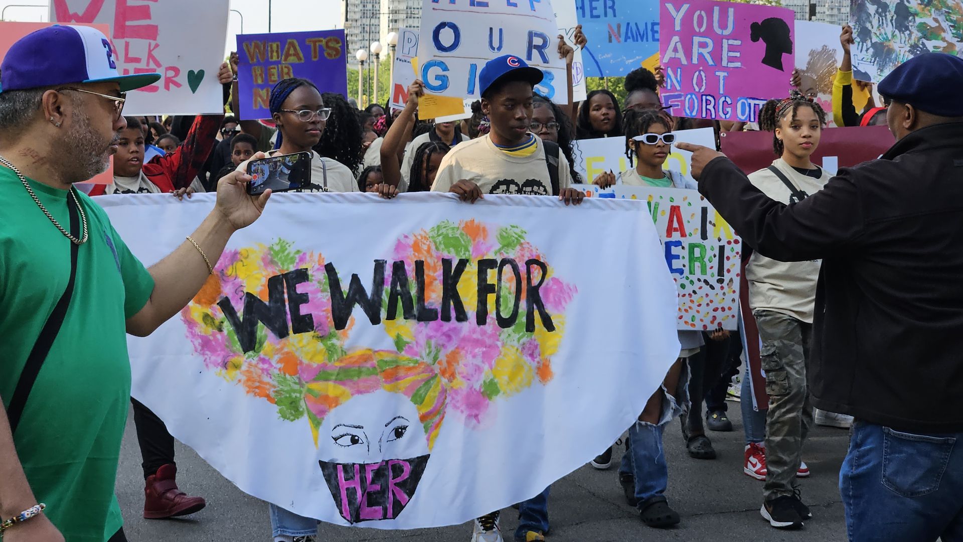 Photo of people marching with a sign that says "We Walk For Her" 