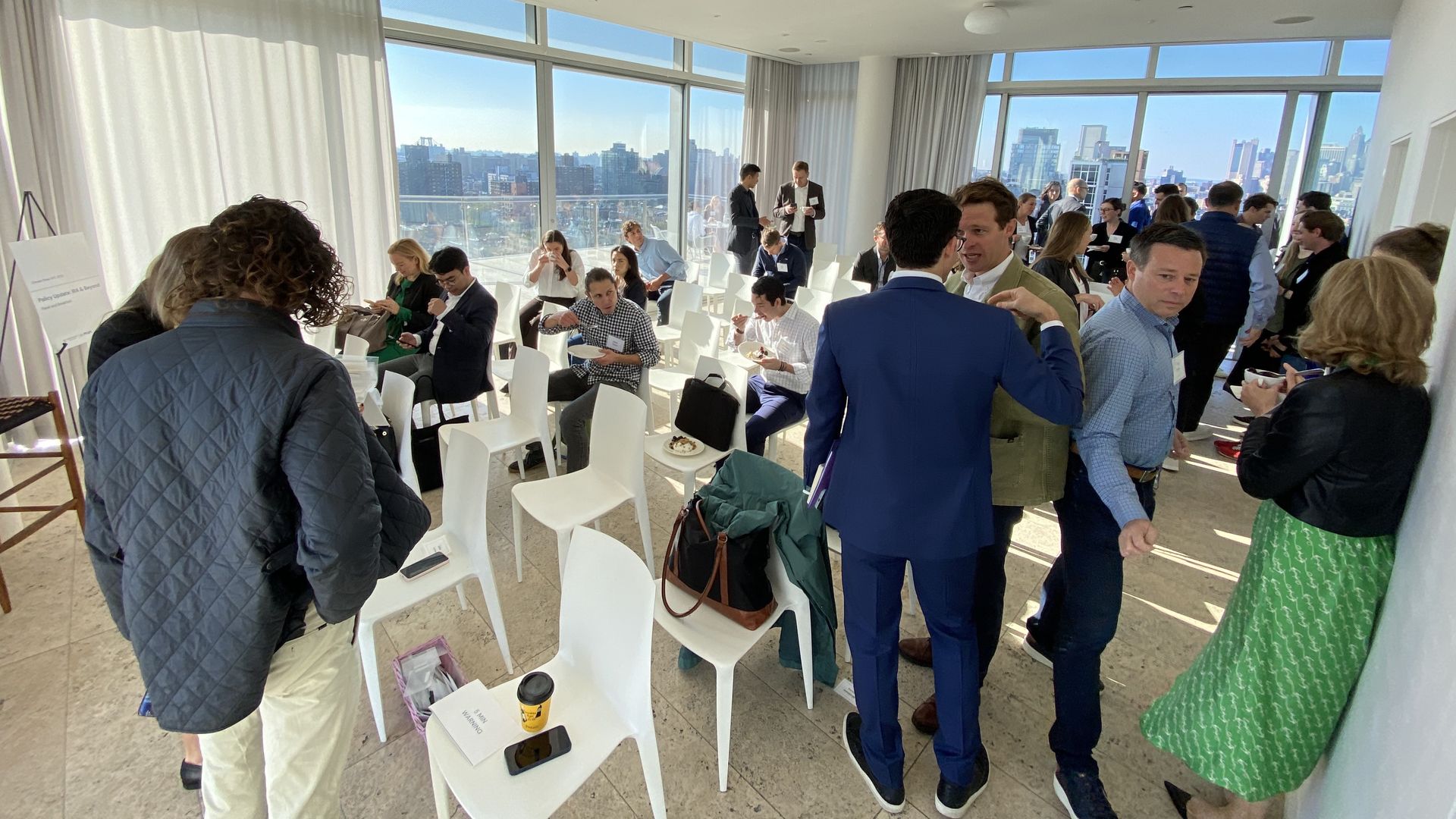 A photo of investors and founders chatting ahead of a panel, amid white chairs and a few white curtains, in a window-filled penthouse in NYC.